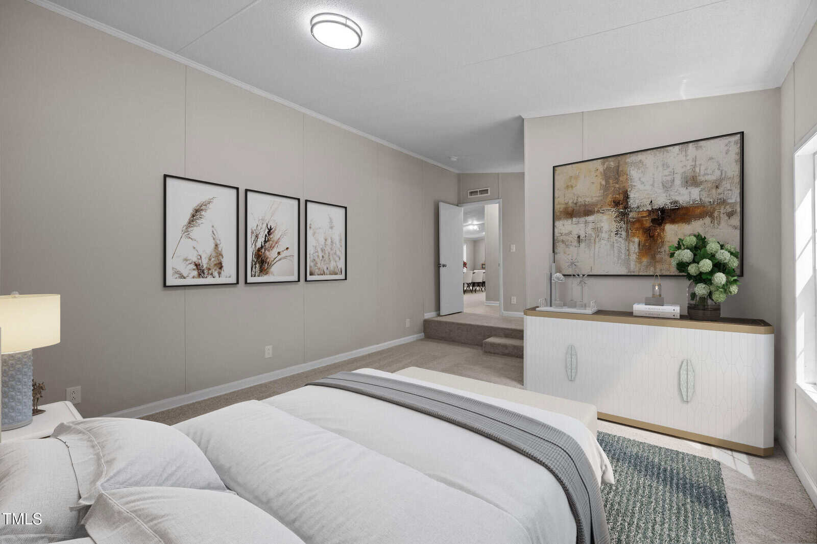 A bedroom with a neatly made bed, light-colored walls, framed art above the bed, a white dresser with a large abstract painting, and a window letting in natural light. The carpet is beige, and a lamp sits on the nightstand.
