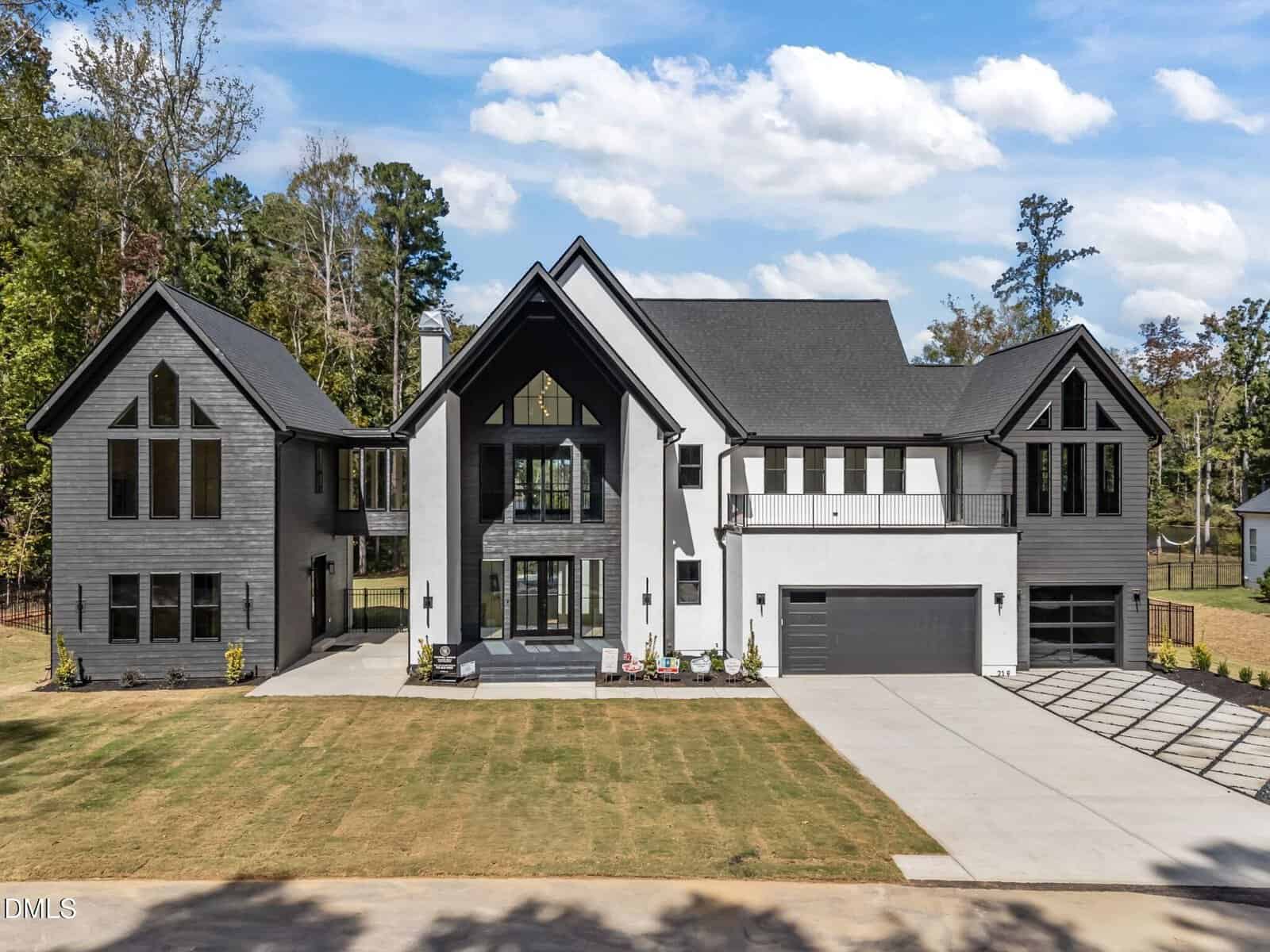 A large modern two-story house with black and white exterior, multiple peaked roofs, large windows, a three-car garage, and a spacious driveway surrounded by lawn and trees.