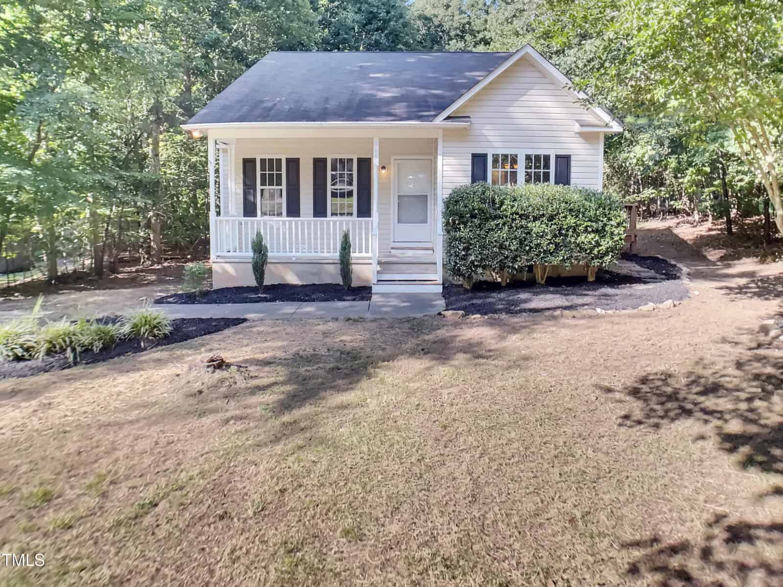 A small, single-story house at 108 Madeline Court in Youngsville features light siding, black shutters, a front porch, and steps leading to a white door. Bushes line the porch, and the front yard is mostly bare with some landscaping. Trees surround the property.