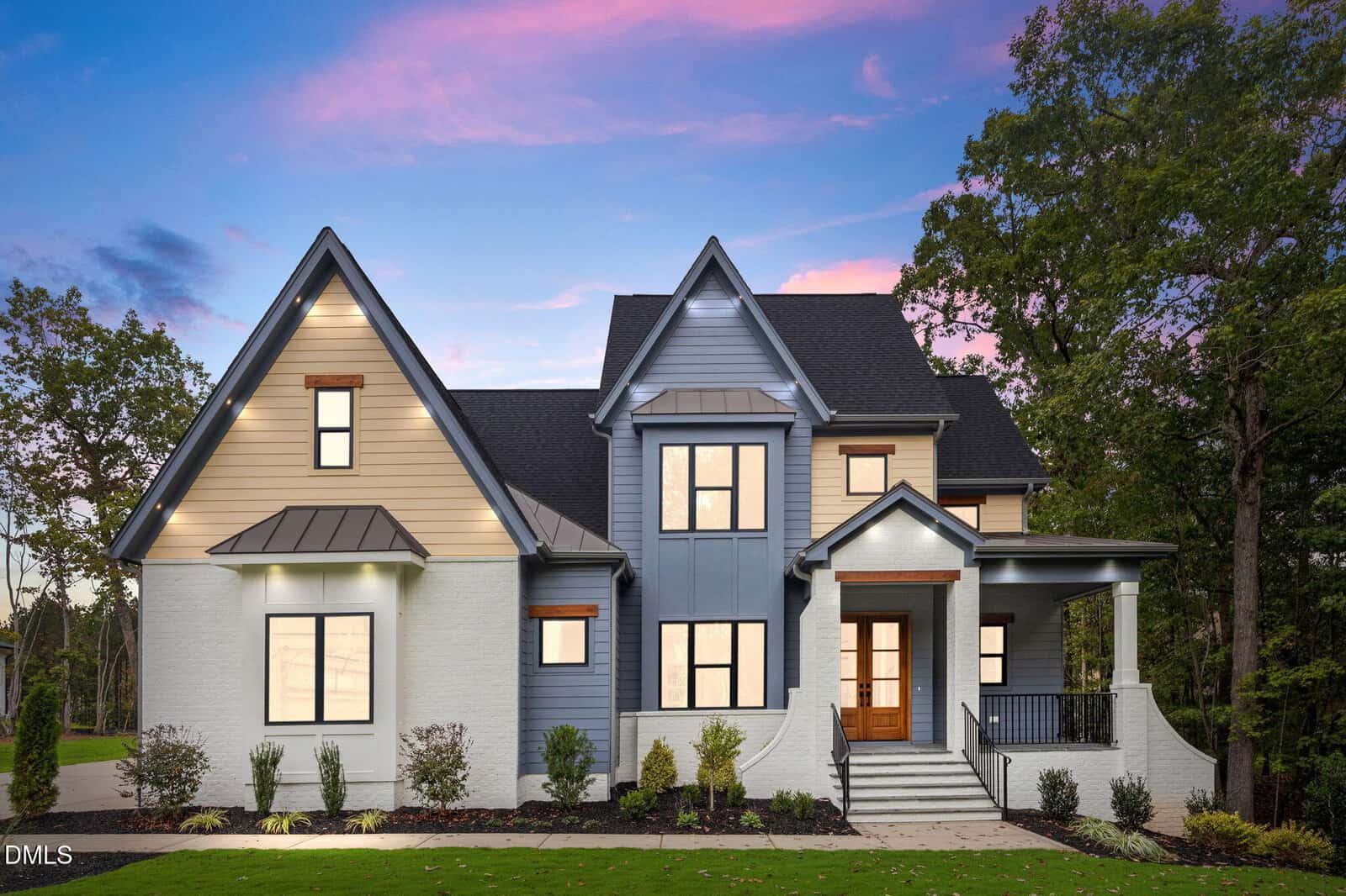 Modern two-story house at 65 Chestnut Oak Drive, Youngsville, with mixed siding in cream and blue-gray, gabled roof, large windows, and a covered front porch, surrounded by manicured shrubs and trees at sunset.