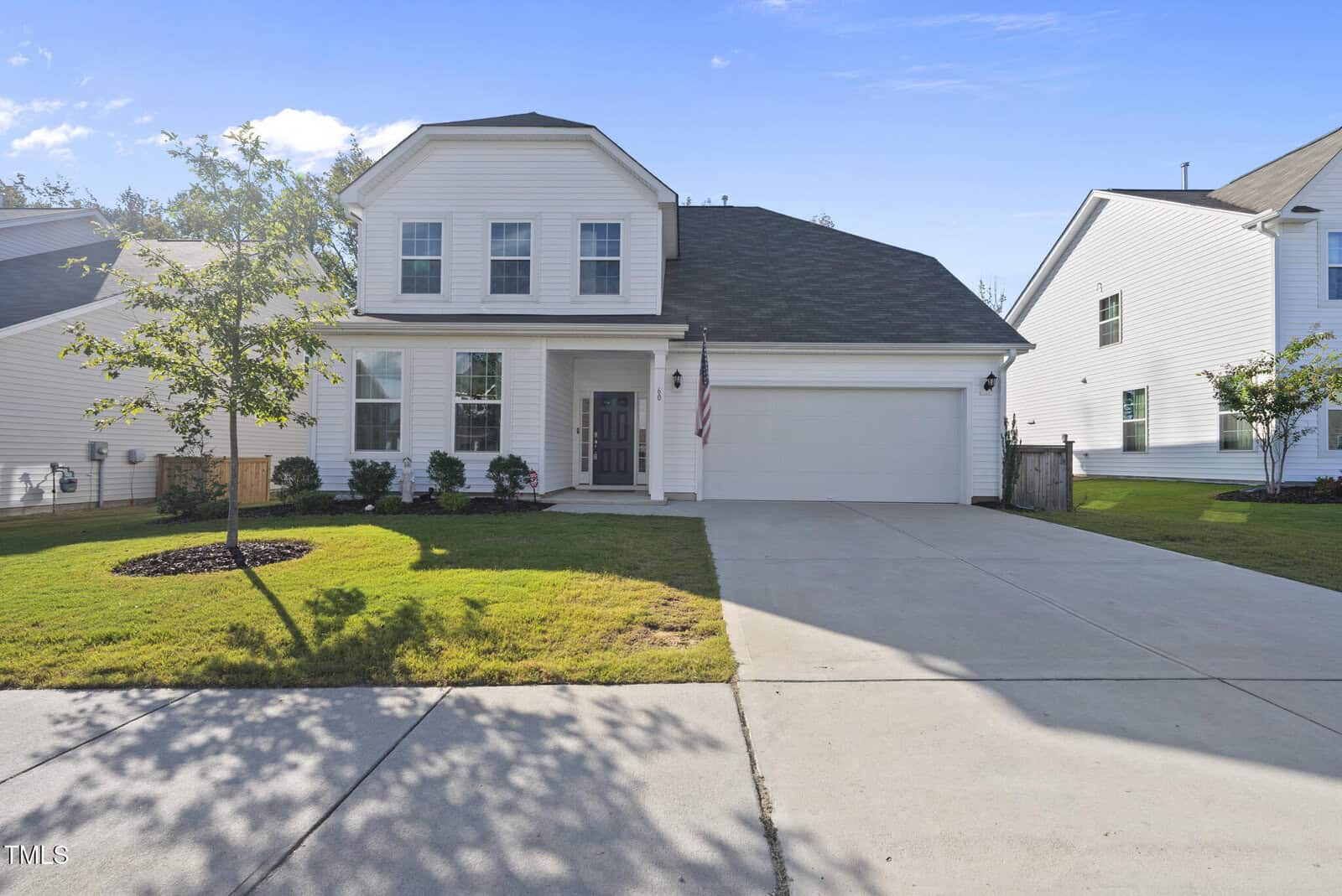Two-story white house with black roof and attached two-car garage, concrete driveway, small front lawn, and a few young trees and shrubs. Located at 60 Silent Brook Trail in Franklinton, the house features four front windows and an American flag by the main entrance.