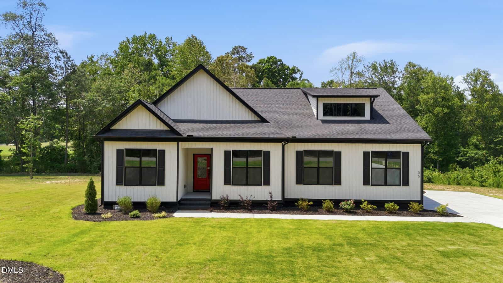 A modern white house with black trim at 35 Autumnwood Lane, Zebulon features a striking red front door, large windows, and a black roof, set on a manicured lawn with mulch beds and trees beneath a clear blue sky.
