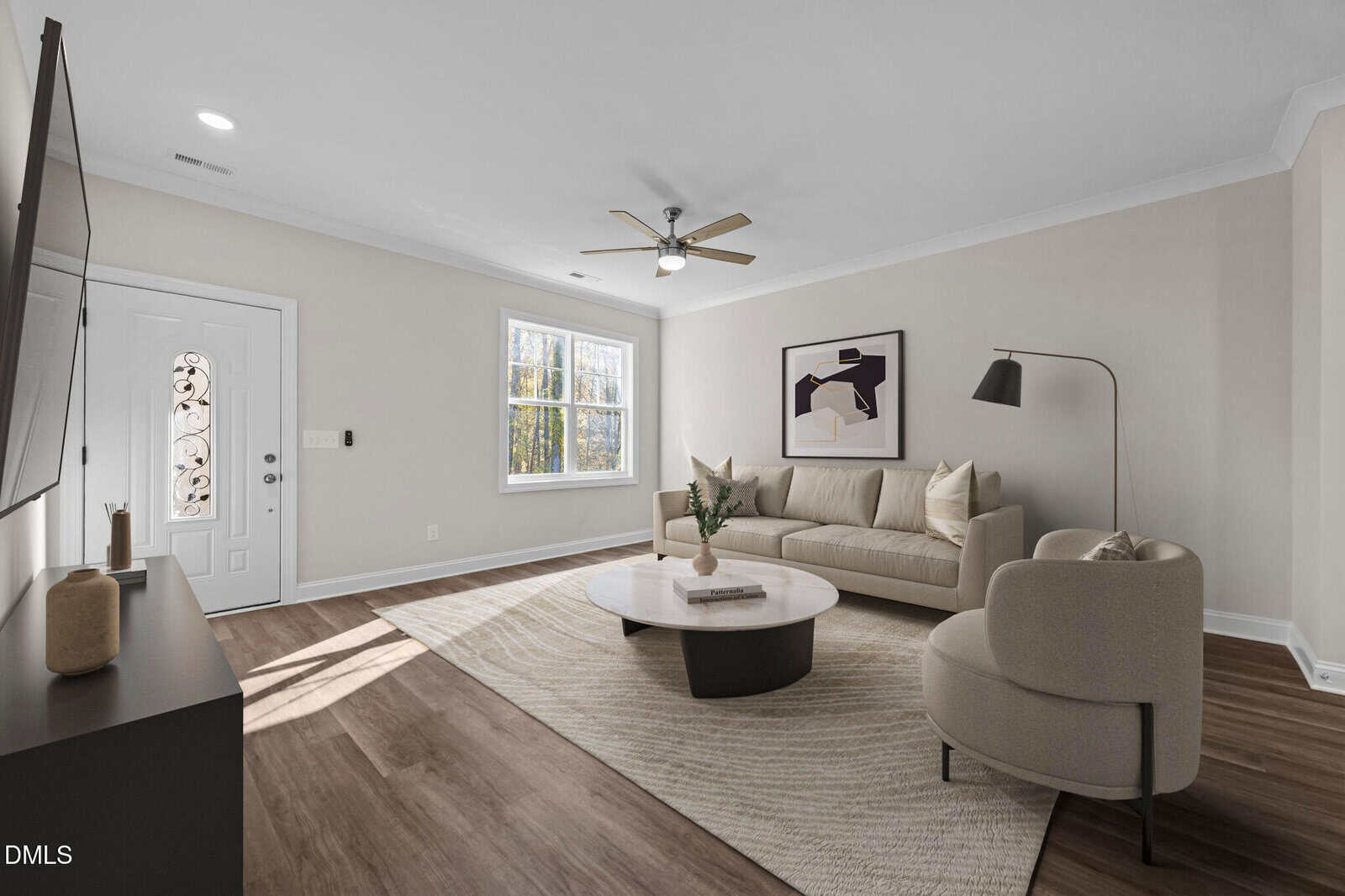 A modern living room with light walls, wood flooring, a beige sofa, round coffee table, armchair, floor lamp, and wall art. Sunlight streams through a window near a white front door.
