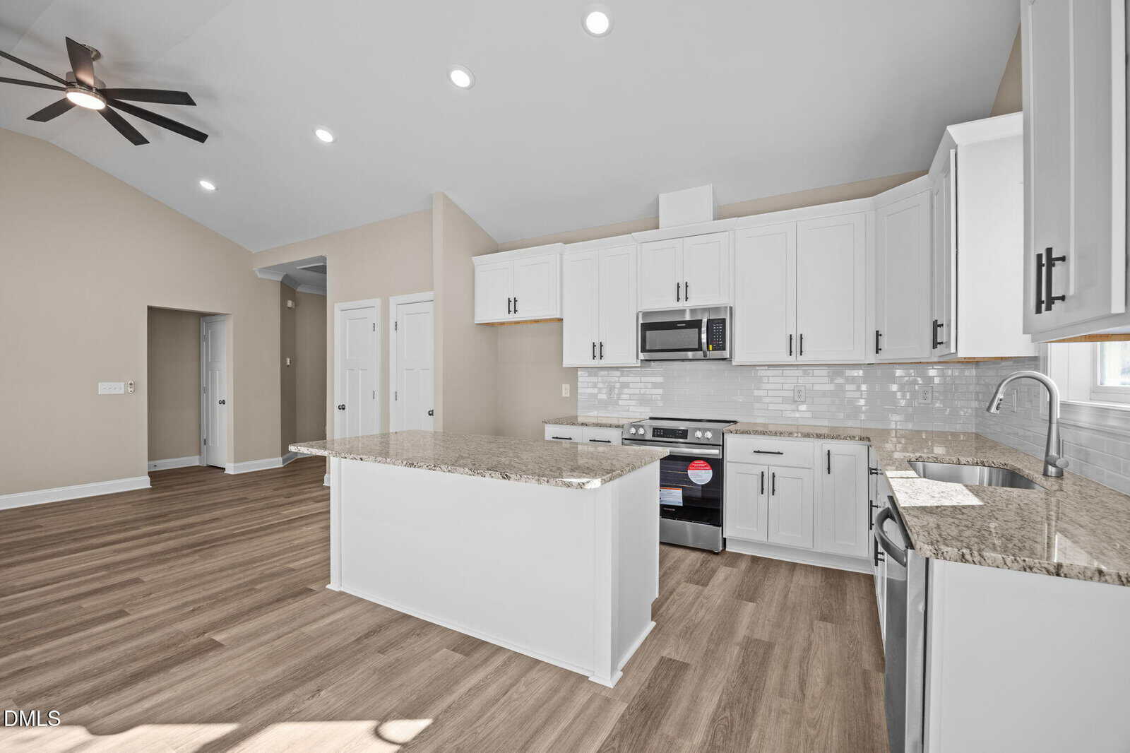Modern kitchen with white cabinets, granite countertops, stainless steel appliances, a center island, wood-style flooring, and neutral-colored walls. Ceiling fan and recessed lighting are visible in the open layout.