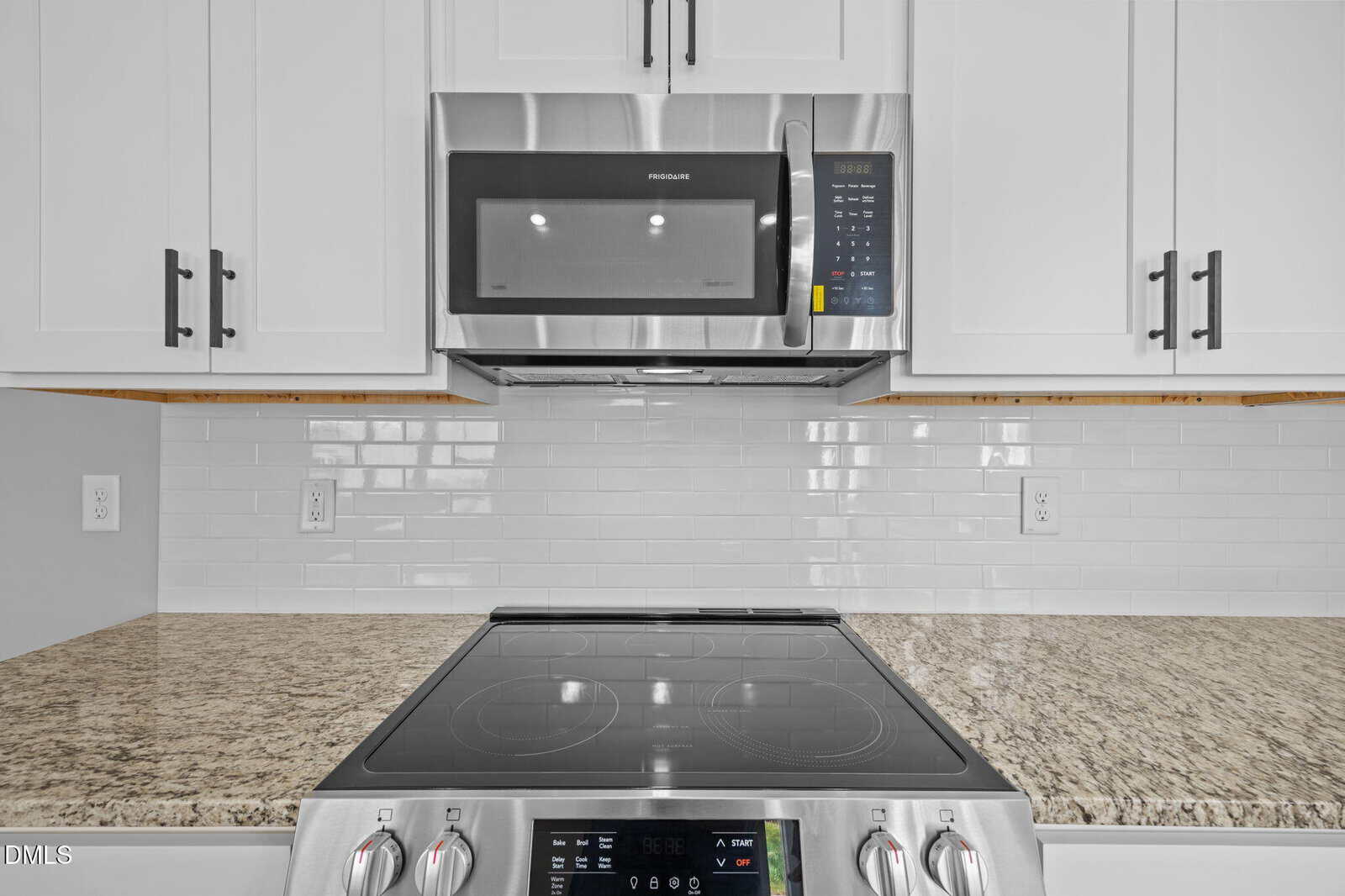 A modern kitchen featuring a glass-top electric stove with control knobs, a built-in stainless steel microwave above it, white cabinets, white subway tile backsplash, and granite countertops.