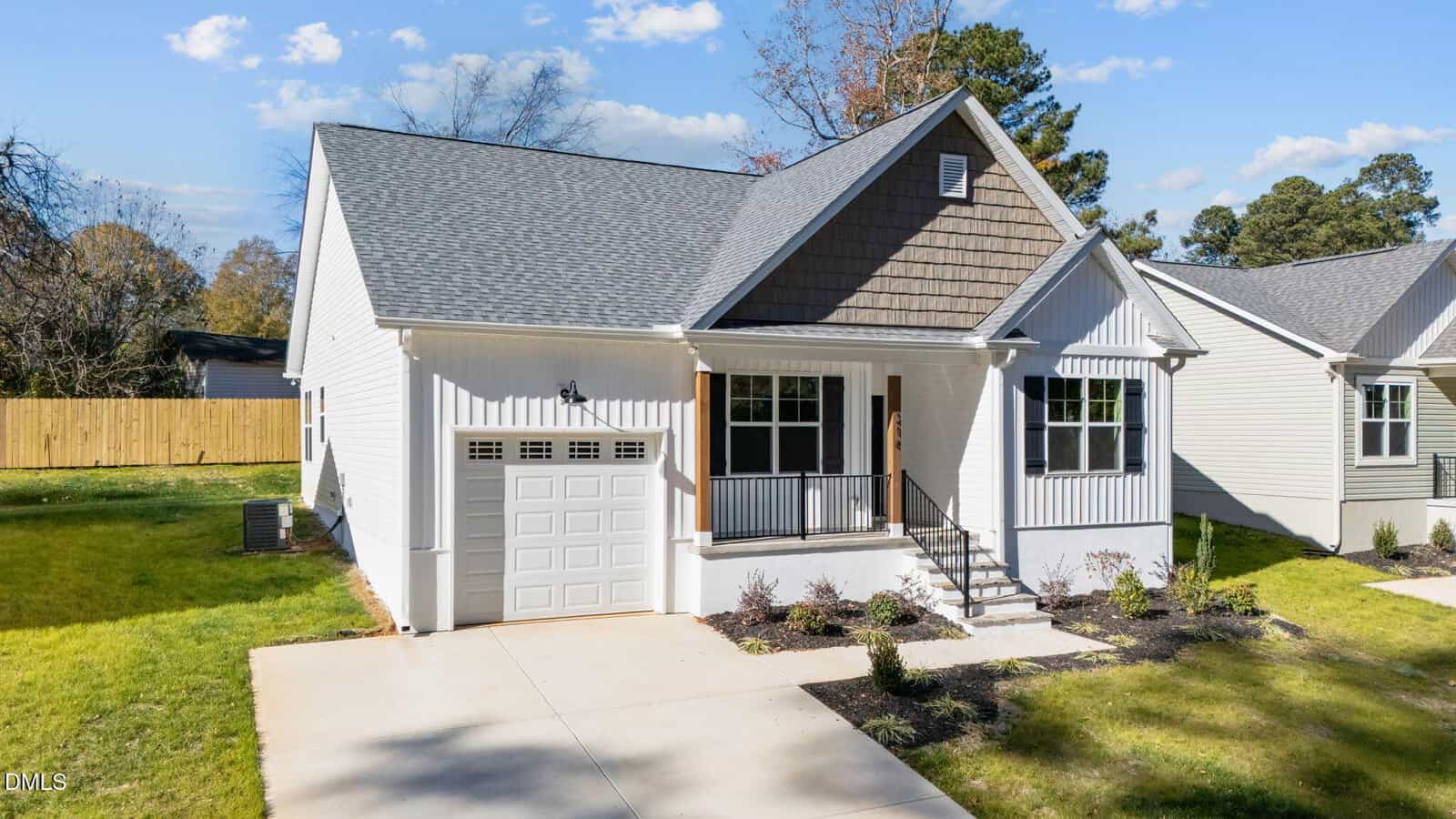 A modern single-story house with gray roof shingles, white siding, a small front porch with black railings, one-car garage, and a neatly landscaped yard under a sunny blue sky.
