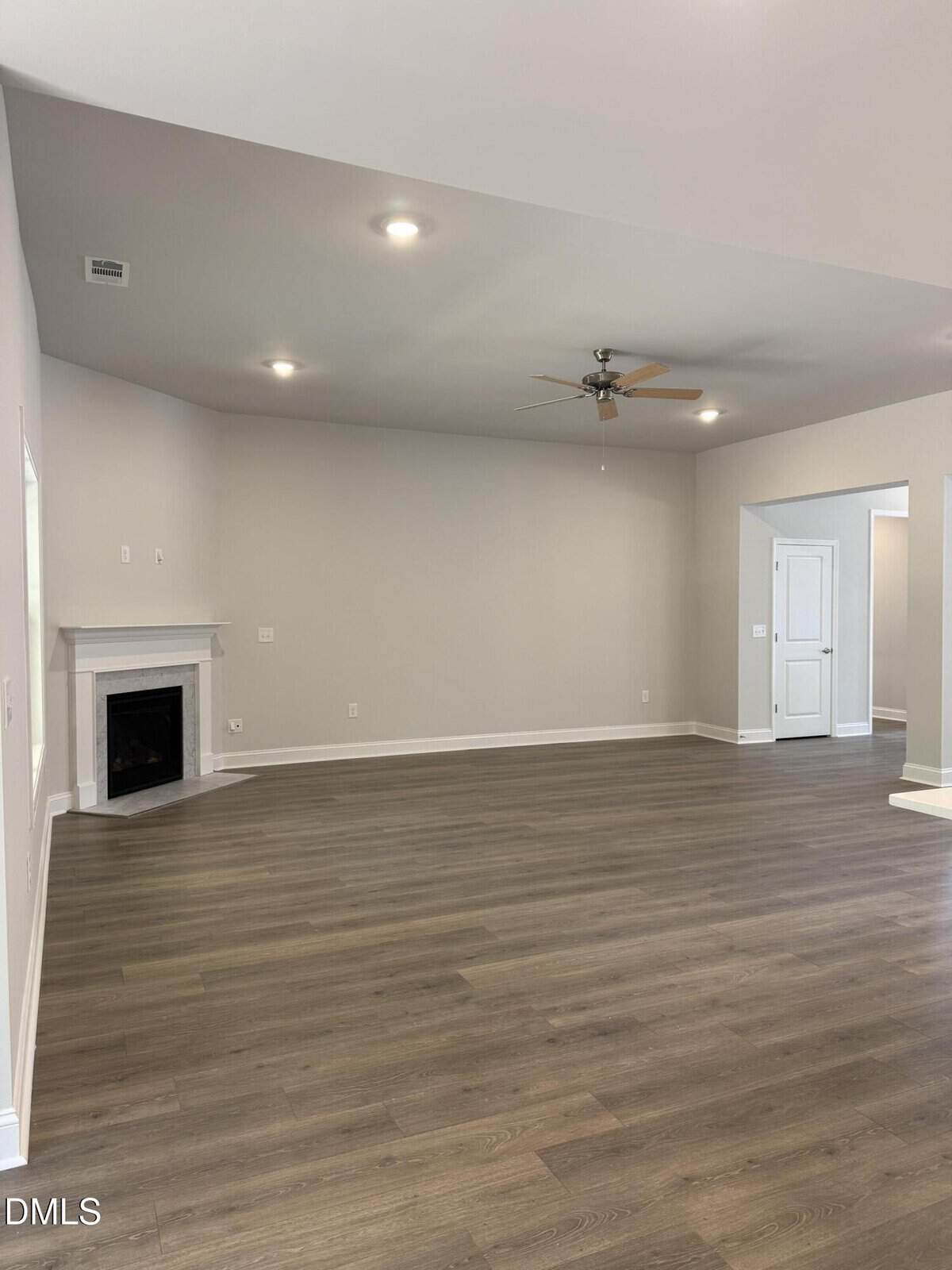 Spacious empty living room with light gray walls, wood-style flooring, recessed lighting, a ceiling fan, and a corner fireplace. There are white doors and trim, and an open doorway to another area.