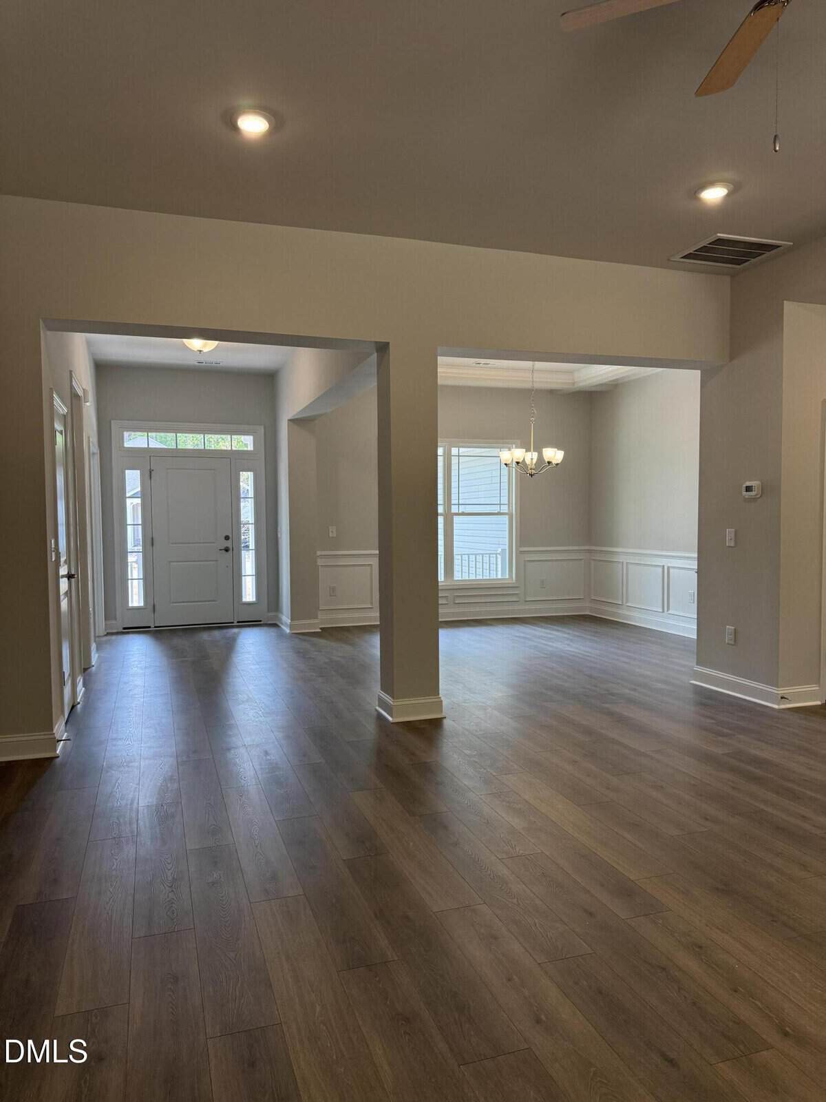 Spacious entryway leading to an open dining area with wood flooring, white walls, wainscoting, chandelier, front door with windows, and recessed ceiling lights.