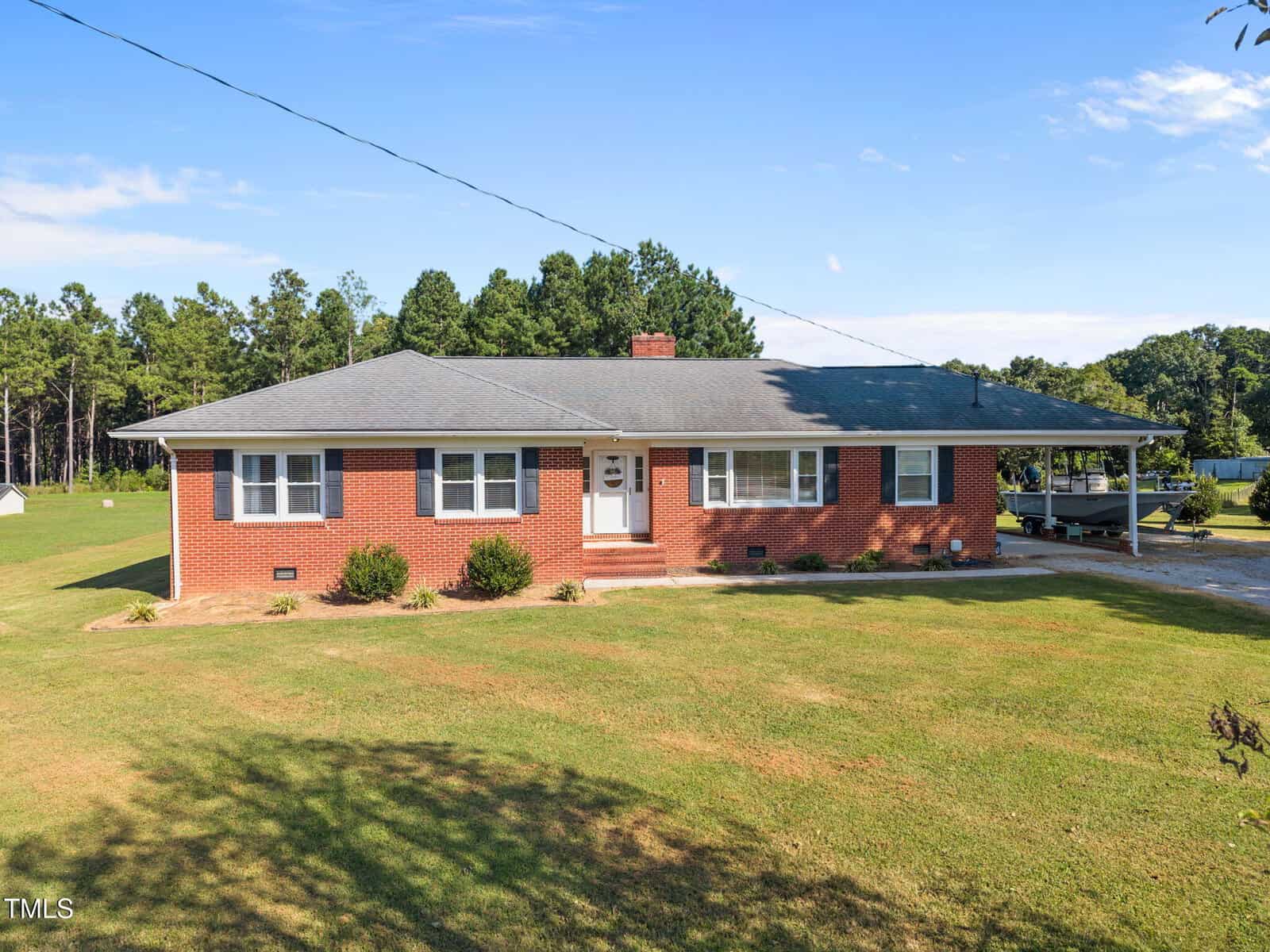 One-story red brick house with gray roof, white trim, and central chimney located at 4572 Antioch Road. It sits on a large grassy yard with a driveway on the right. Trees and blue sky are visible in the background, offering classic Oxford charm.