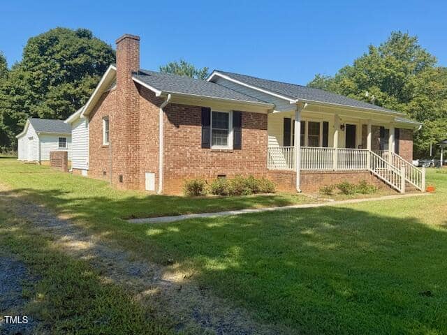 Charming single-story brick house at 6527 US 15, Oxford, featuring a covered front porch with white railing and gabled roof. Surrounded by lush grass and trees, it also includes a small outbuilding and a concrete path to the porch steps.