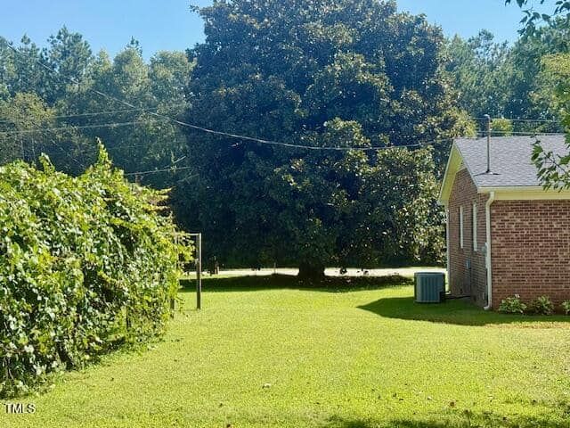 A grassy backyard with a brick house on the right, a large tree in the background, a hedge on the left, and overhead utility lines crossing the yard. An air conditioning unit is next to the house.
