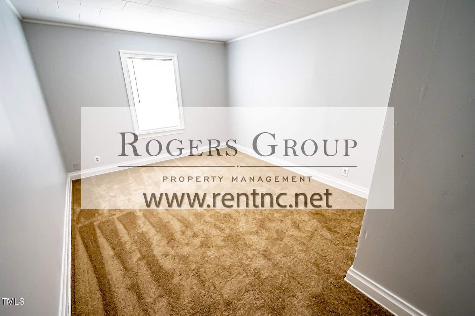Empty room with white walls, a beige carpet, and a single window letting in natural light. Large watermark text in the center reads "Rogers Group Property Management www.rentnc.net".