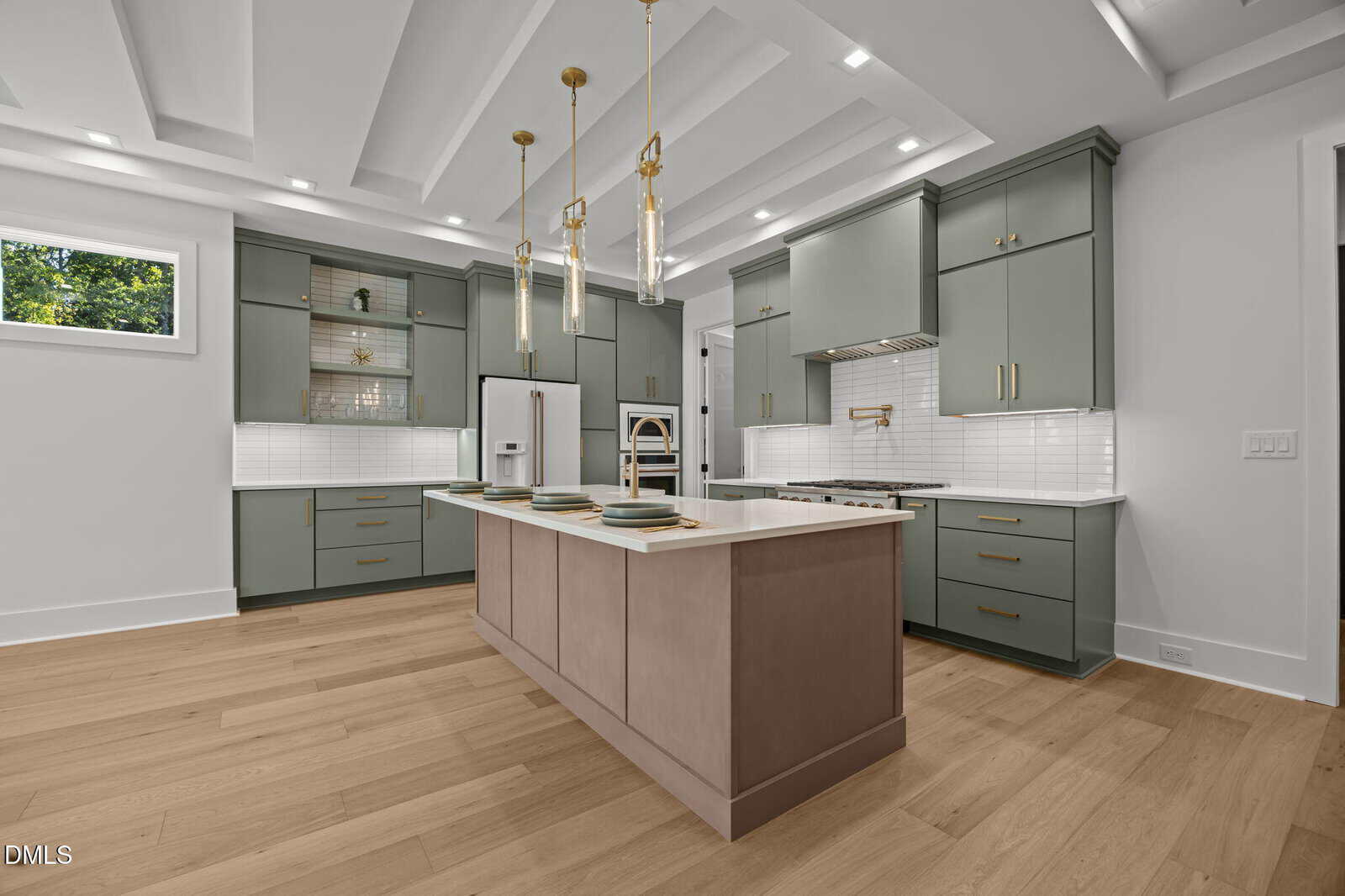 Modern kitchen with sage green cabinets, a light wood floor, a large island with beige base and white countertop, three gold pendant lights, white subway tile backsplash, and built-in appliances.