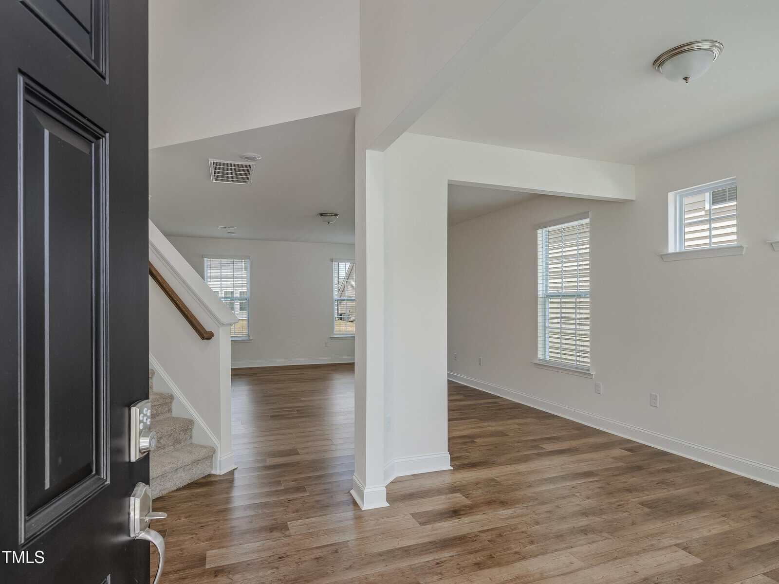 Open black front door showing a bright interior with light walls, wood flooring, a staircase with carpeted steps on the left, and windows letting in natural light in the entryway and living room area of 60 Copperleaf Court Court, located in desirable Franklinton.