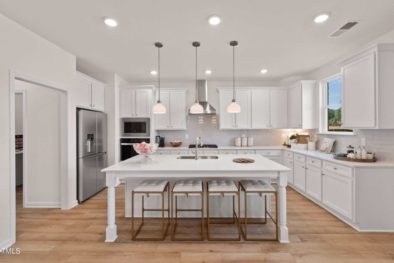 Modern kitchen at 260 Sugar Pine Drive, Franklinton, featuring white cabinets, stainless steel appliances, a large island with three wooden stools, pendant lights overhead, and light wood flooring. The countertop is clear except for a bowl and some minimal decor.
