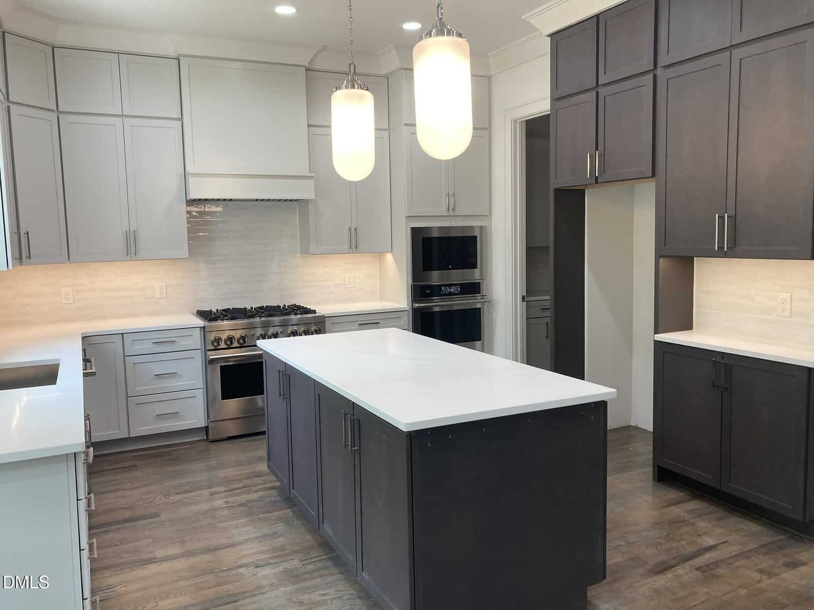 Modern kitchen with dark and light cabinets, a large white island, stainless steel appliances, pendant lights, white backsplash, and wood floors.