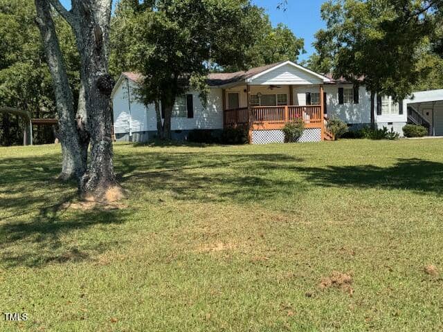 A white, single-story house with a red porch sits on a grassy lawn surrounded by trees under a clear blue sky.