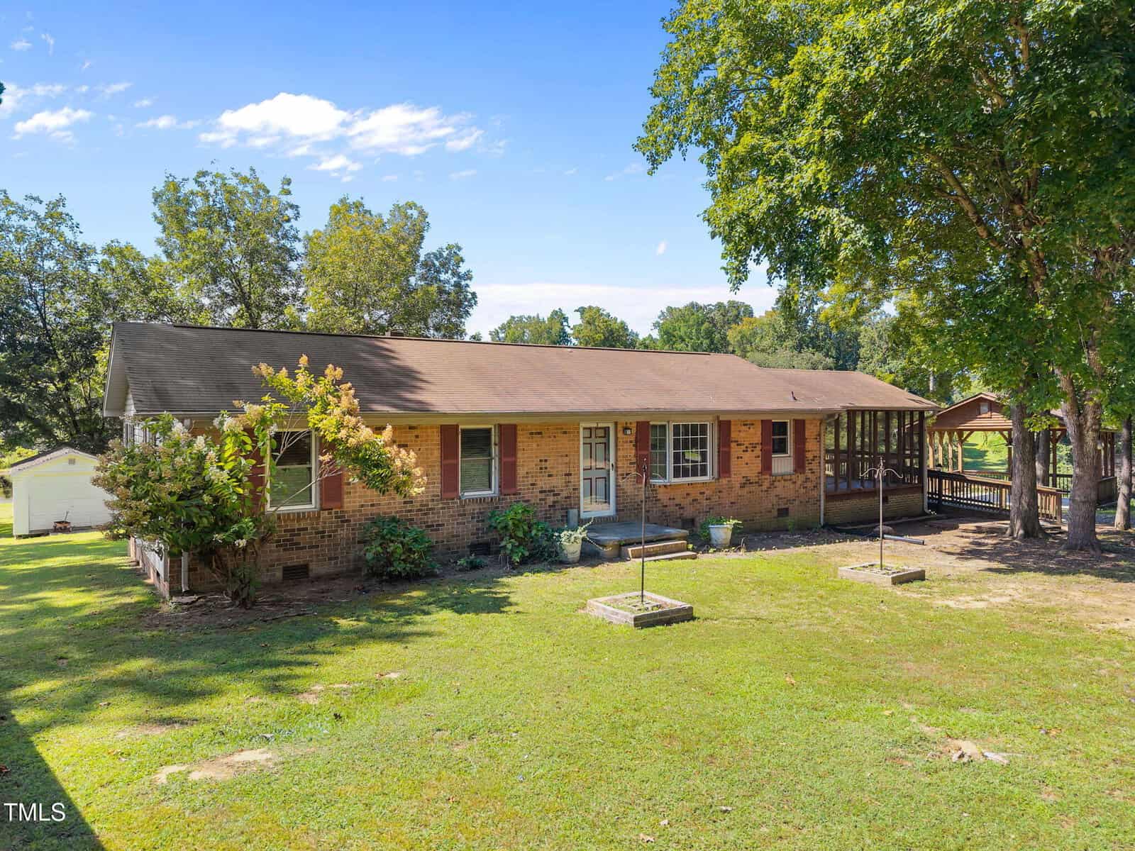 Charming single-story brick house at 4642 Fielding Knott Road, Oxford, with a brown roof, white front door, and several windows. The yard features green grass, a few trees, and a wooden ramp to the side entrance under blue skies.