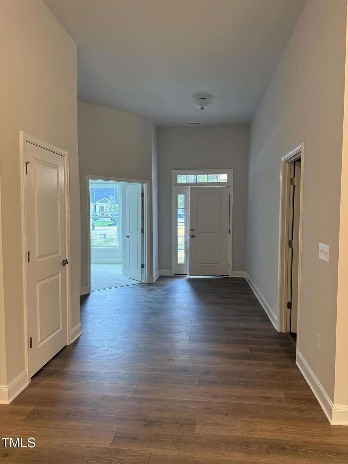 A view of a home’s entryway with light-colored walls, double front doors with glass panels, two side doors, and wood-style flooring. Daylight is visible through the front. Ceiling light fixture is present.