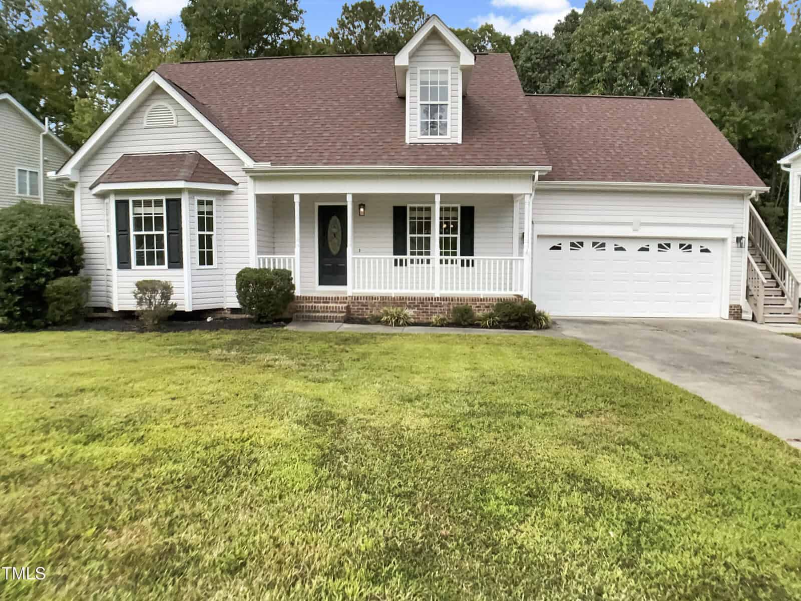 Charming white, single-story house at 2561 Mint Julep Drive in Creedmoor, featuring a covered front porch, attached two-car garage with brown roof, lush green lawn, mature trees, and a concrete driveway leading to the garage.
