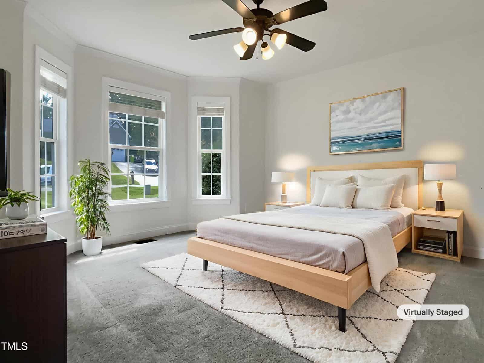 A bedroom with a wooden bed, white bedding, two nightstands with lamps, a large window, a ceiling fan, a potted plant, and a framed picture above the bed. The room is virtually staged.