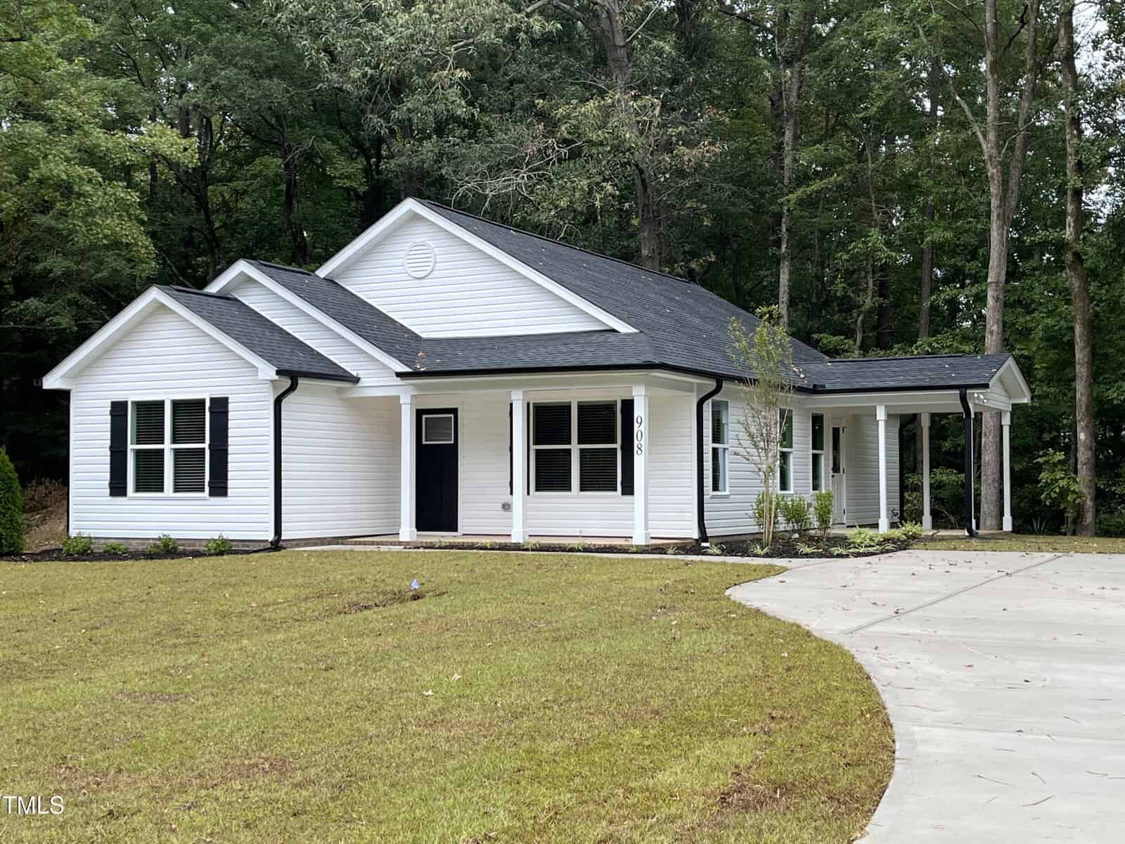A single-story white house with black trim at 908 Circle Drive in Creedmoor features a covered front porch and attached carport, nestled beside a curved concrete driveway amid grass and tall trees.