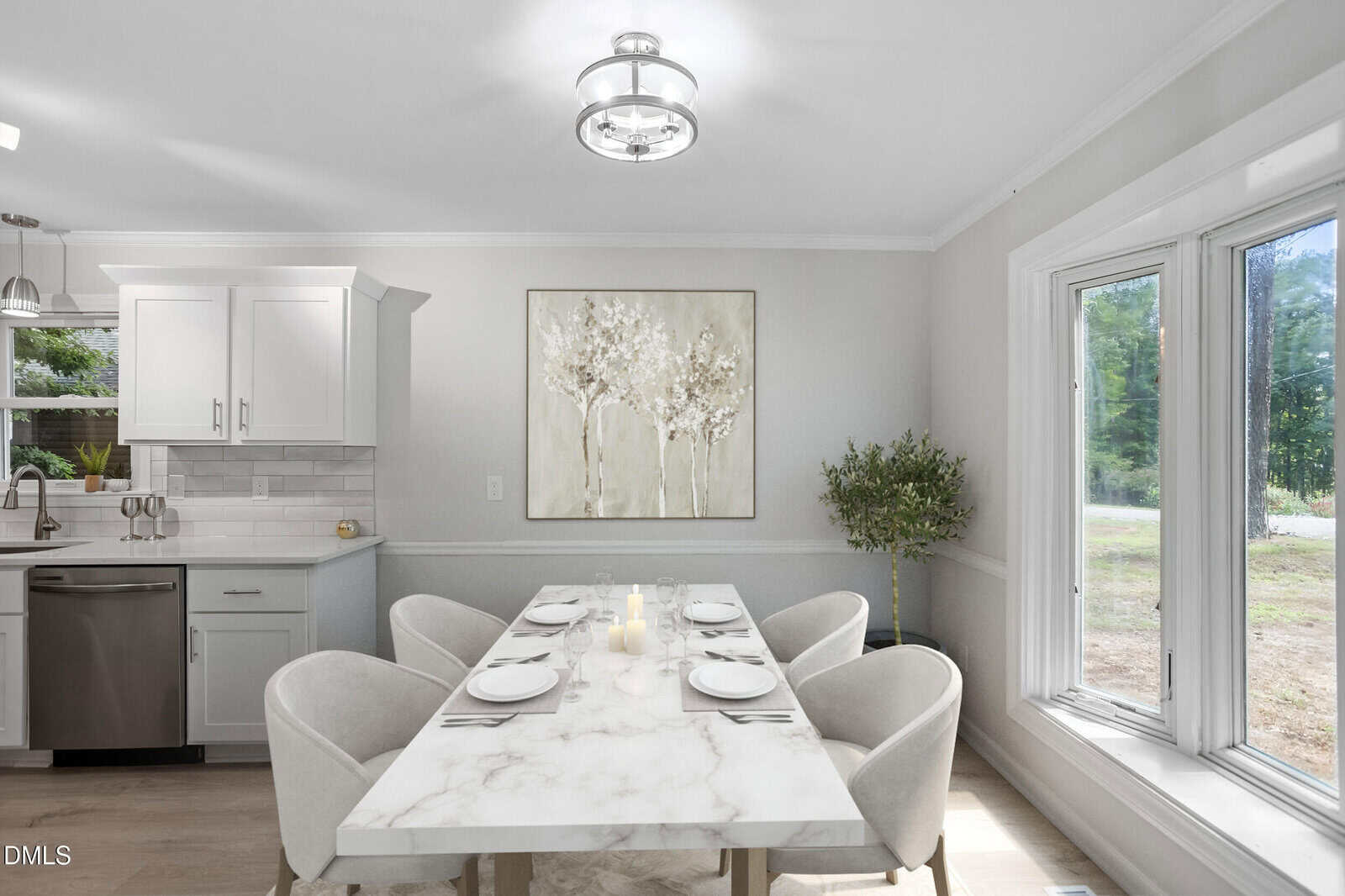A modern dining area with a marble table set for four, beige chairs, a potted plant, wall art, and large windows letting in natural light from outside. The space is bright with white walls and cabinetry.