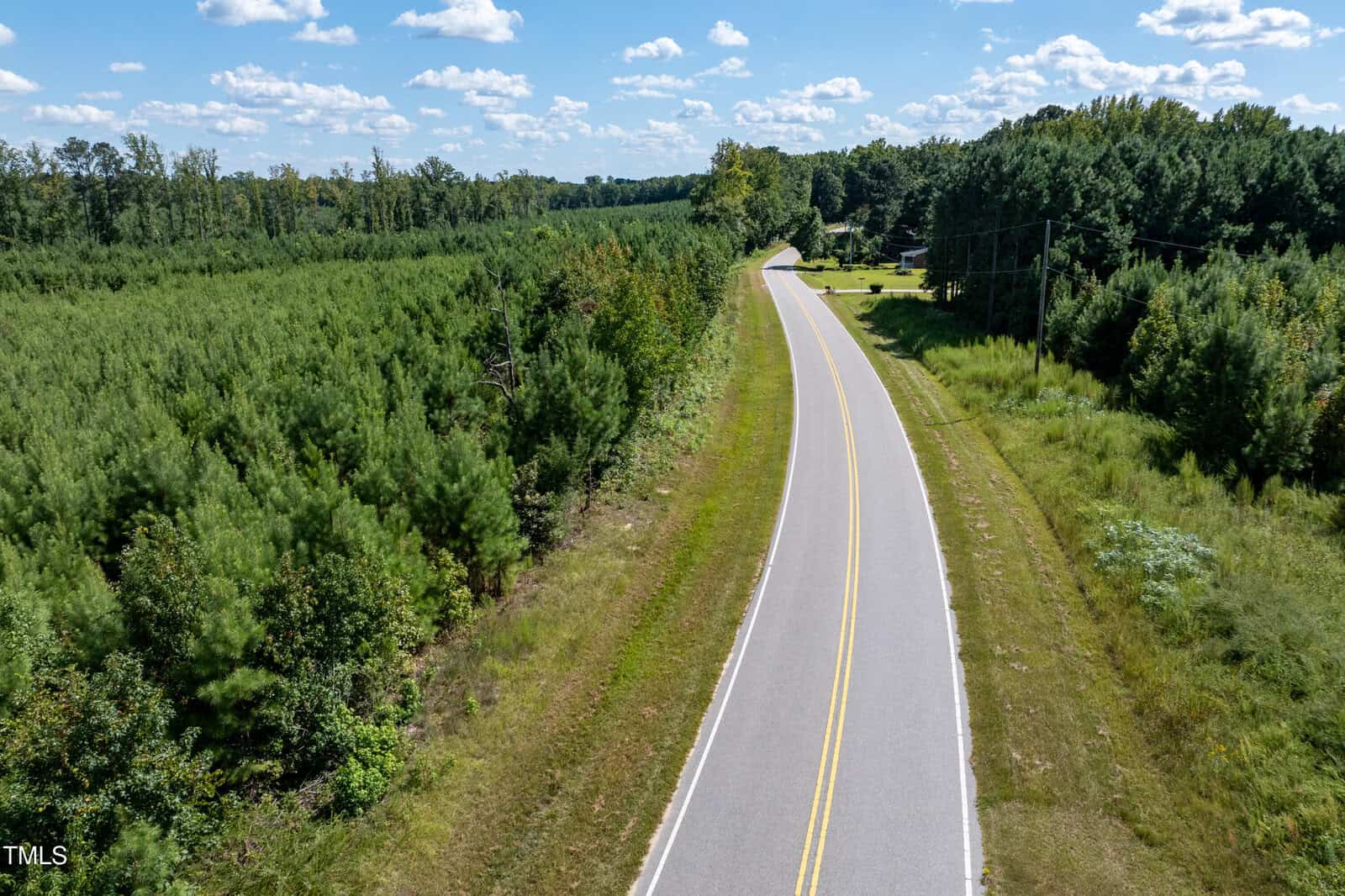 A two-lane rural road, #3&4 Walter Grissom Road, curves through a green forested area near Kittrell under a blue sky with scattered clouds. Power lines run alongside the road, and a few buildings are partially visible in the distance.