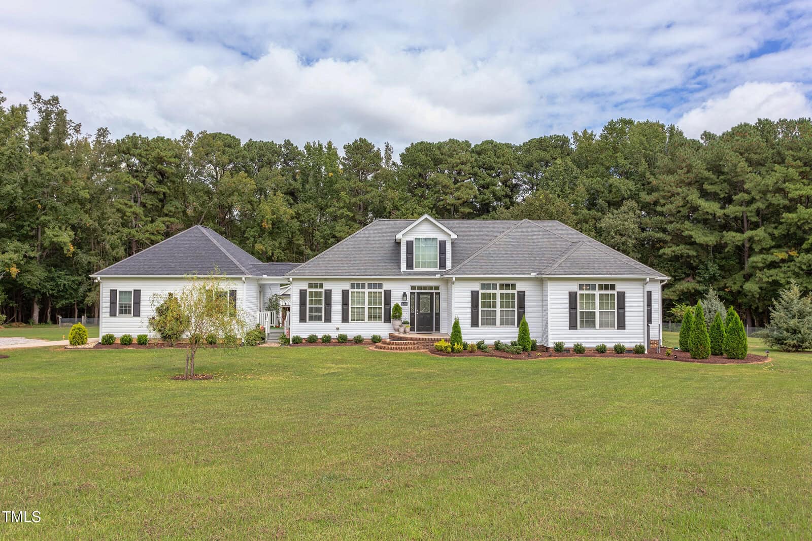 Charming single-story white house with gray roof at 4191 Bobbitt Road, Kittrell; features an attached garage on the left, central front steps, multiple windows, and a large grassy yard framed by trees and a cloudy sky.