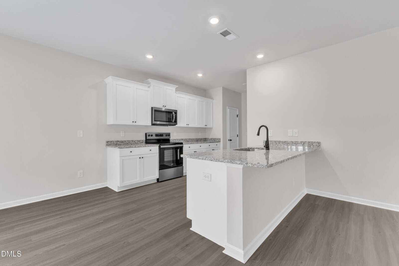 A modern kitchen with white cabinets, stainless steel appliances, granite countertops, and an island with a black faucet. The space has recessed lighting and light wood flooring.