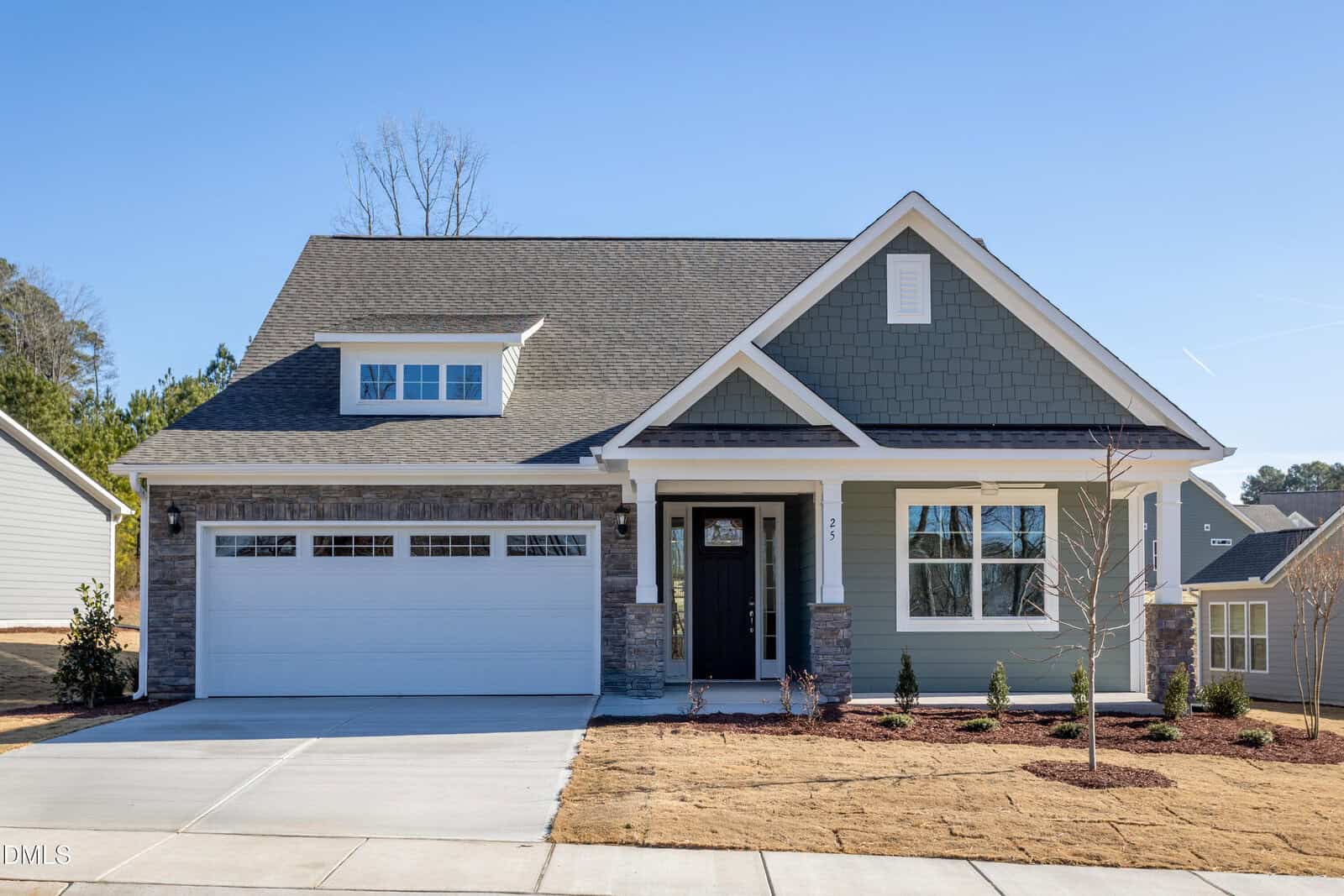 A modern single-family house in Youngsville with gray-green siding, stone accents, a covered front porch, white trim, and a two-car garage. Located at 25 Sawtooth Oak Lane, it features new landscaping and a concrete driveway.