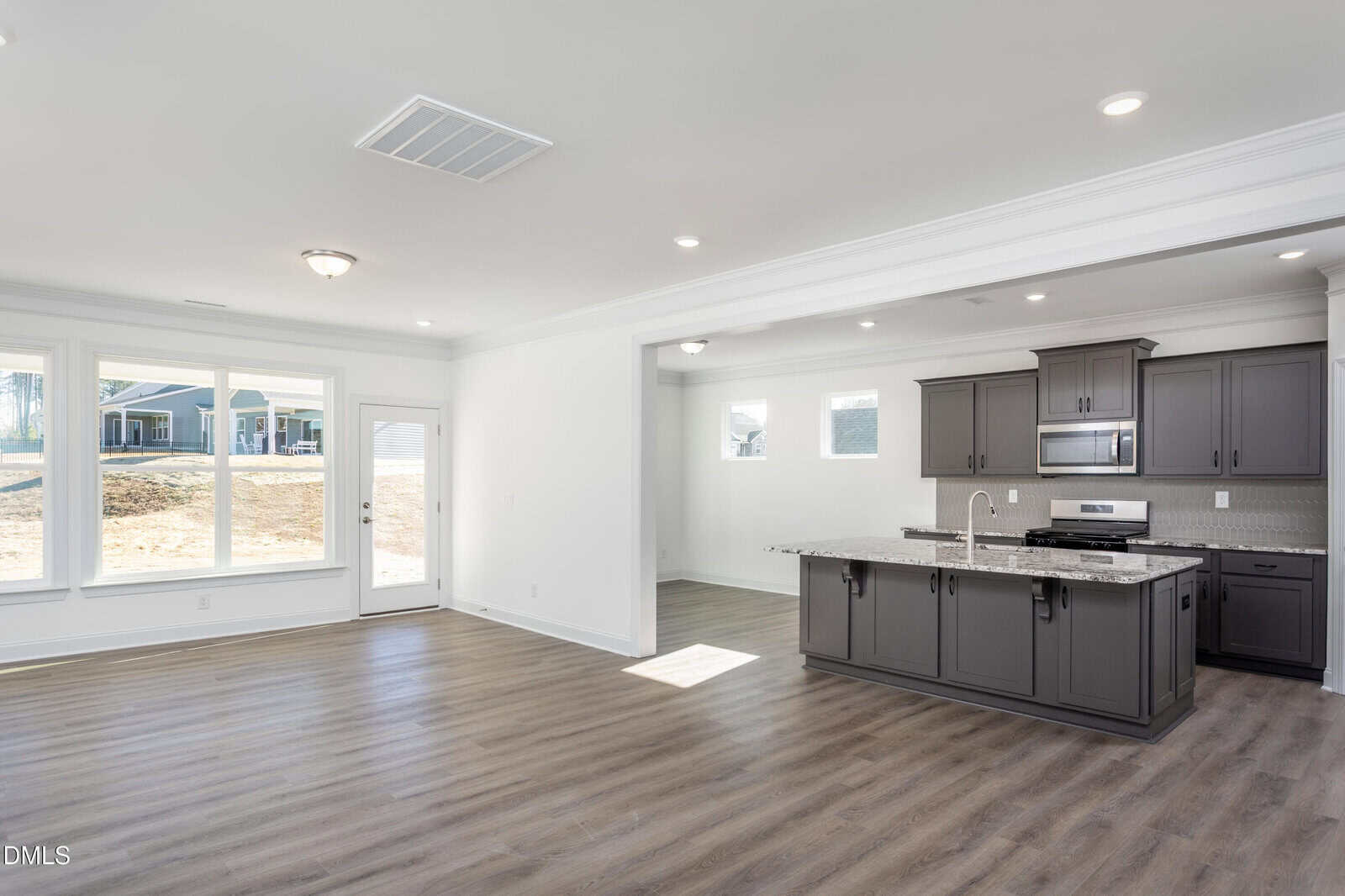 Bright, modern open-concept kitchen and living area with gray cabinets, stainless steel appliances, a large island, wood-style flooring, and large windows letting in natural light.