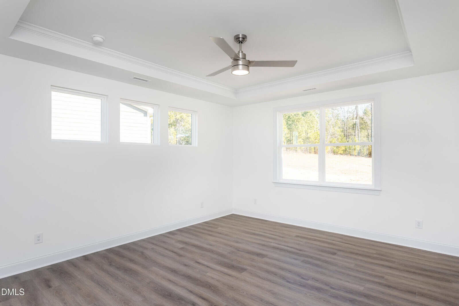 Bright, empty room with light gray walls, wood flooring, three small windows, one large window, and a ceiling fan with light.
