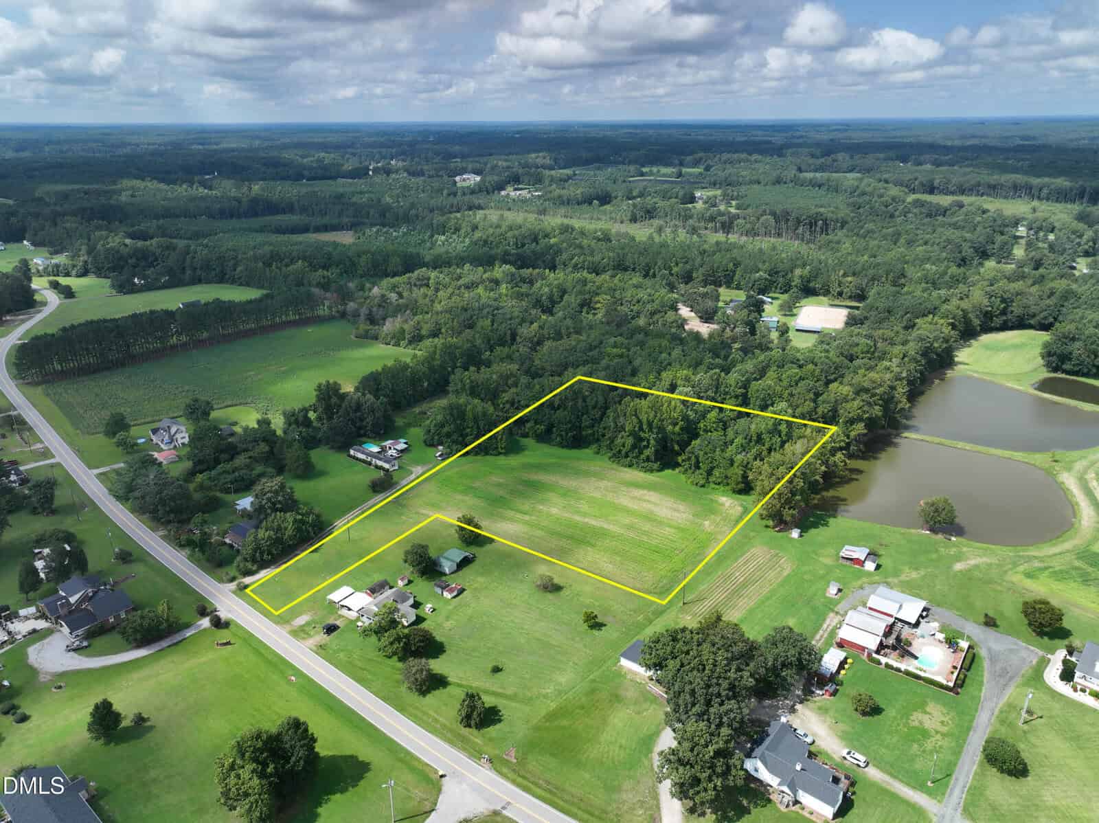 Aerial view of a rural landscape near Louisburg with fields, trees, and several houses. A rectangular section of land at 0 Wood Road is outlined in yellow near a pond, surrounded by greenery and open spaces, with a road running along the bottom left.