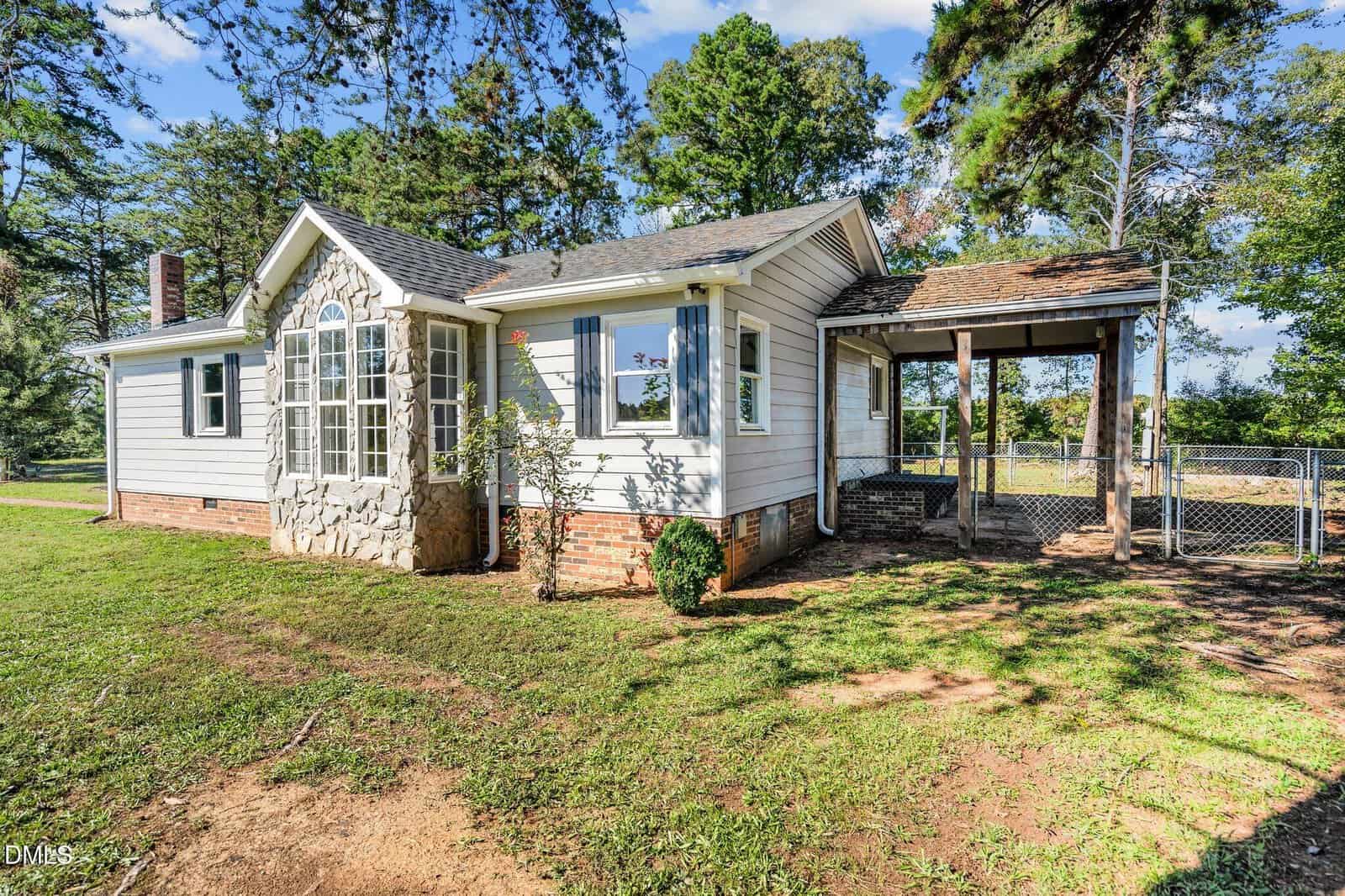 A single-story house at 4193 Ji Oakes Road with white siding, brick foundation, and a stone accent around arched windows; an attached covered porch with steps and a fenced yard, surrounded by trees in Bullock.
