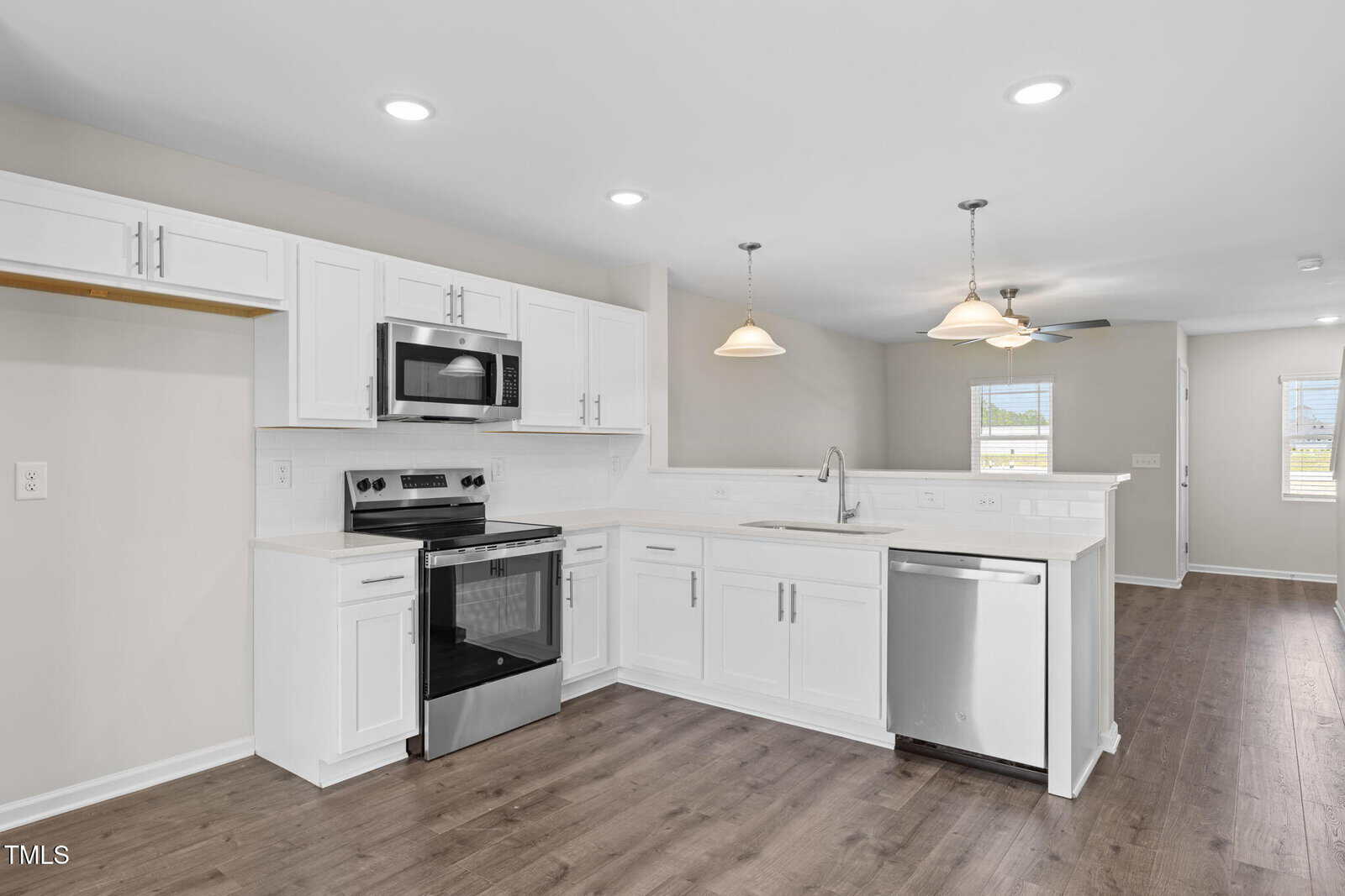Modern kitchen with white cabinets, stainless steel appliances, electric stove, microwave, dishwasher, double sink, and light wood flooring. Open layout connects to dining and living areas with ceiling fans and pendant lights.