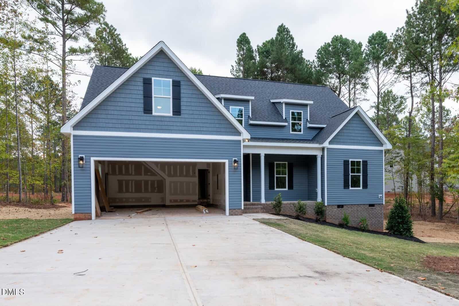 A newly built, two-story blue house with white trim, a gable roof, and an attached double garage sits on a concrete driveway at 175 Purslane Drive in Franklinton. The garage doors are open, and the construction appears unfinished. Trees surround the property.