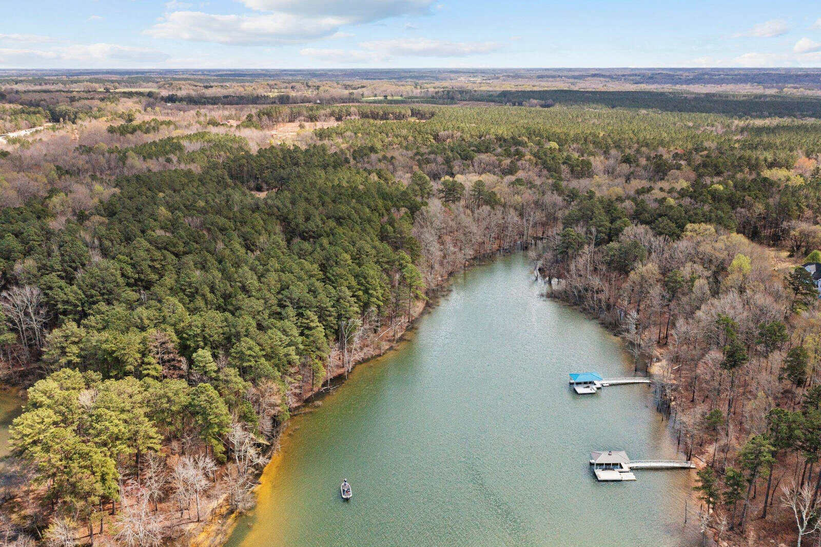 Aerial view of a forested lakeshore with two docks extending into the water, a boat near the shore, and vast green trees surrounding the calm lake.