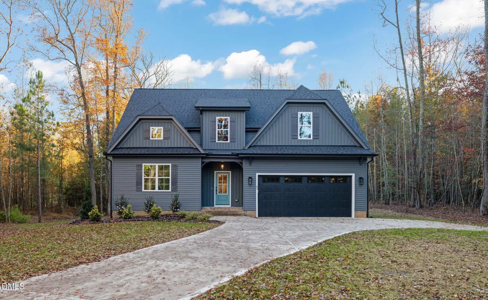 Two-story modern house with dark gray siding, a covered front porch, and an attached two-car garage. Located at 45 Beauview Way in Zebulon, the home is surrounded by trees, with a curved concrete driveway and fallen leaves on the lawn.