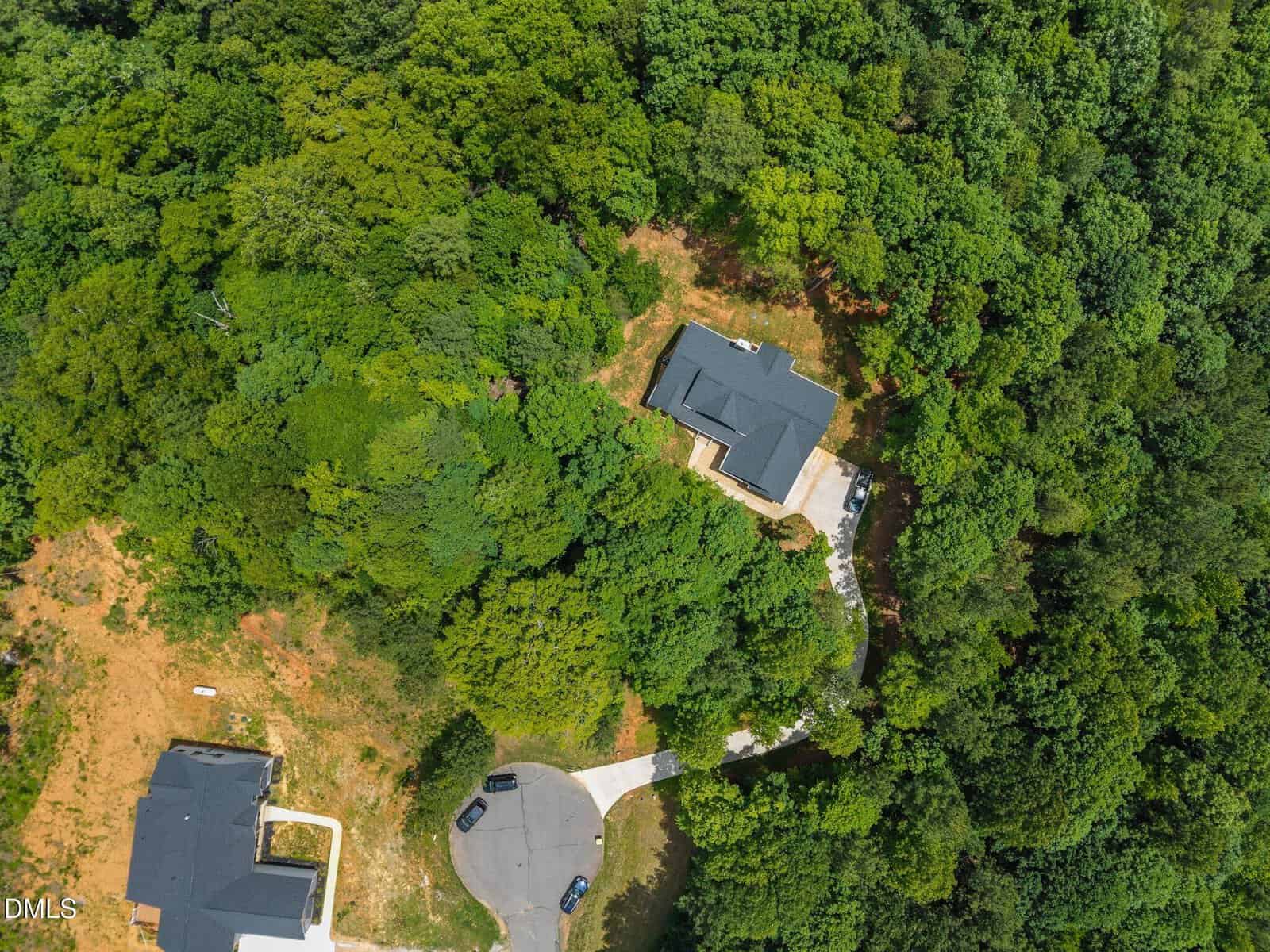 Aerial view of two houses surrounded by dense green trees, located at the end of a cul-de-sac with cars parked on the street, and a winding driveway leading to one house.