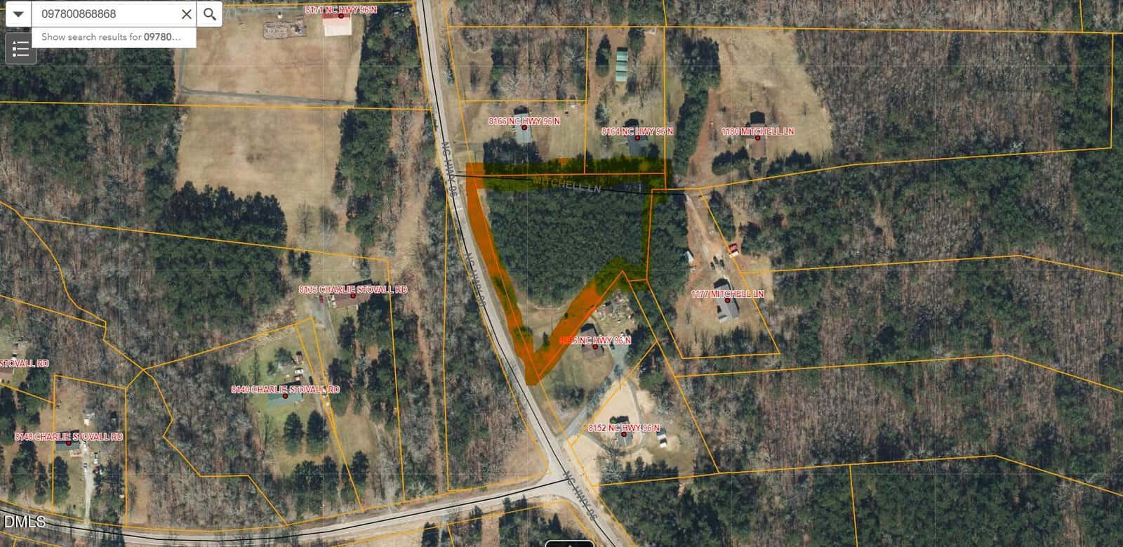 Aerial view of a wooded, triangular parcel of land outlined in orange, surrounded by properties marked with white and red labels. Yellow boundary lines mark adjacent parcels; some buildings and roads visible nearby.