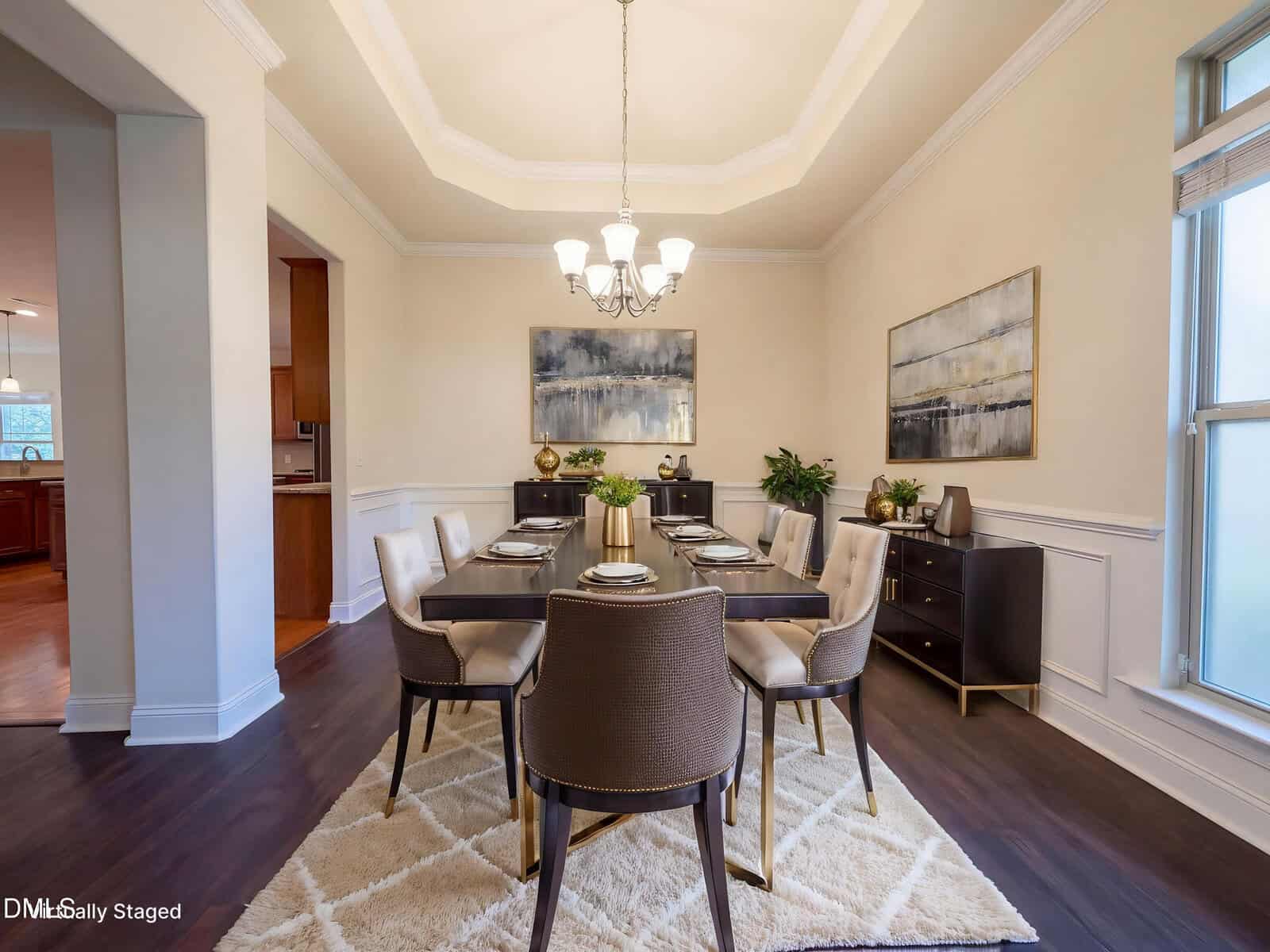 Elegant dining room with a dark wood table set for six, modern chairs, two buffets with decor, neutral walls, abstract art, chandelier, and a large window letting in natural light.