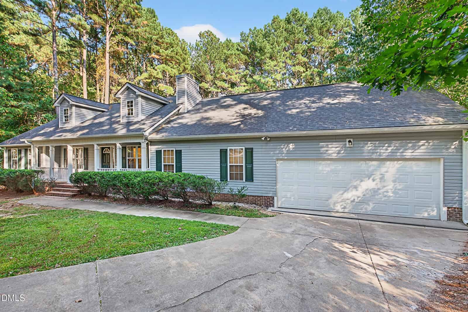 Single-story house with gray siding, white trim, front porch, attached two-car garage, driveway, and green shrubs at 15 Castlerock Drive in Youngsville. Tall trees and blue sky are visible in the background.