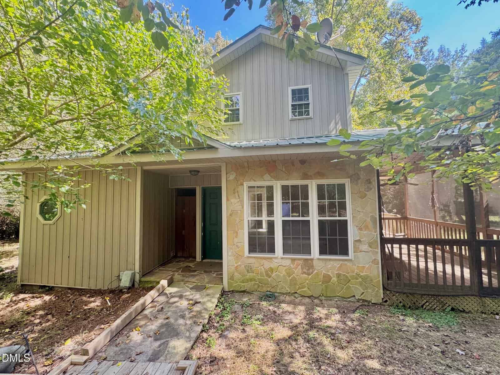A two-story house with stone and wood siding, located at 38 Scarlet Circle in Franklinton, features a green front door, multiple windows, and a pathway leading to the entrance. Surrounding trees create shade and a wooden ramp extends to the right side of the house.