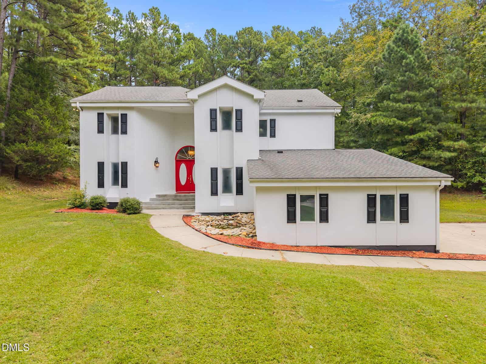 A two-story white house with black shutters and a red front door at 141 Southerland Place in Henderson, surrounded by grass and trees. The curved driveway leads to landscaped areas with rocks and mulch near the entrance.