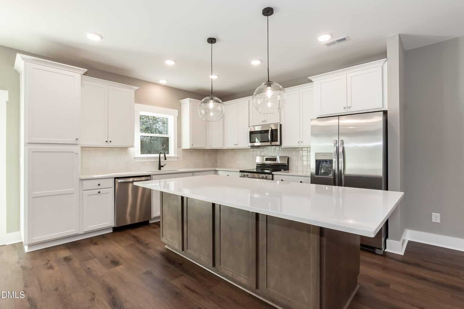 Modern kitchen with white cabinets, stainless steel appliances, a large island with a white countertop, pendant lights, tile backsplash, and dark hardwood flooring.