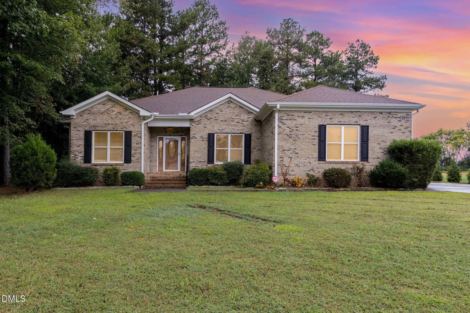 A single-story brick house at 412 Eagle Court, Henderson, features black shutters, a brown front door, and a small set of stairs leading to the entrance, set against a backdrop of trees and a pink and purple sunset sky.
