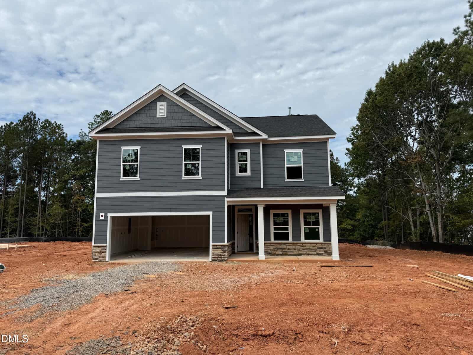 This two-story gray house with white trim and a double garage is situated at 20 Turnberry Court in Franklinton. Nestled on a lot with red dirt and surrounded by trees, the home features multiple windows, a welcoming porch, and some construction materials nearby.