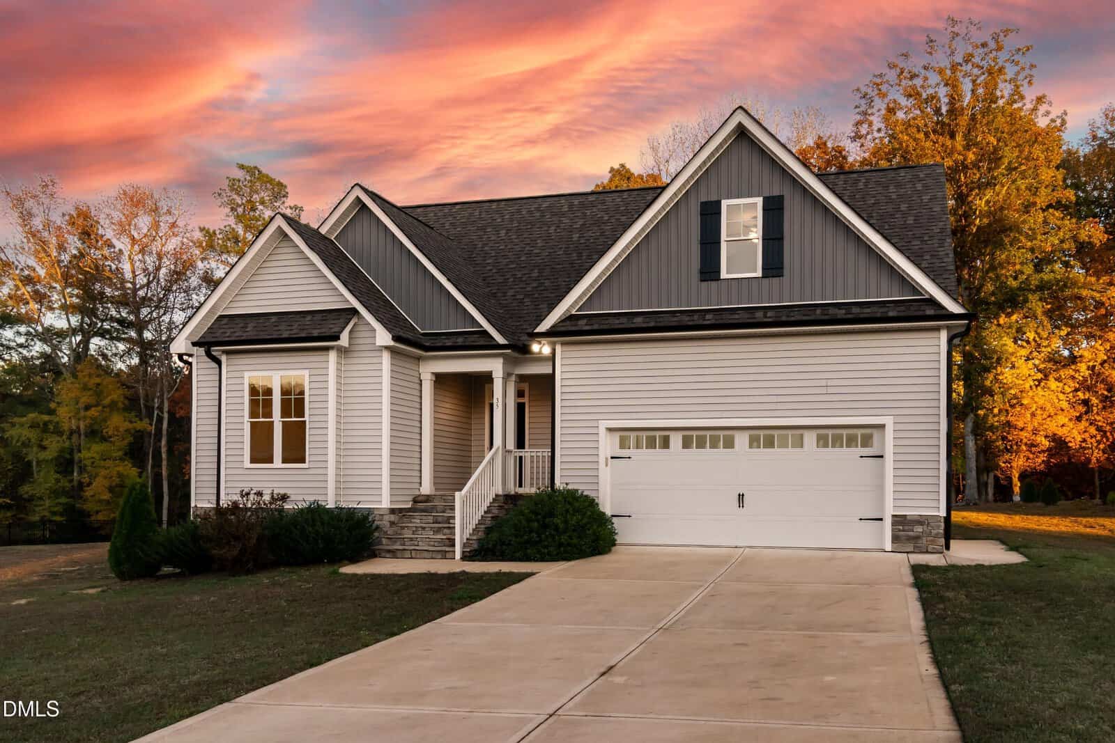 Single-story white house with black trim, a covered front porch, and a two-car garage located at 35 Courtland Drive in Louisburg. A concrete driveway leads to the garage. Trees with autumn foliage surround the home, while the sky above is brushed with vibrant orange and pink clouds.
