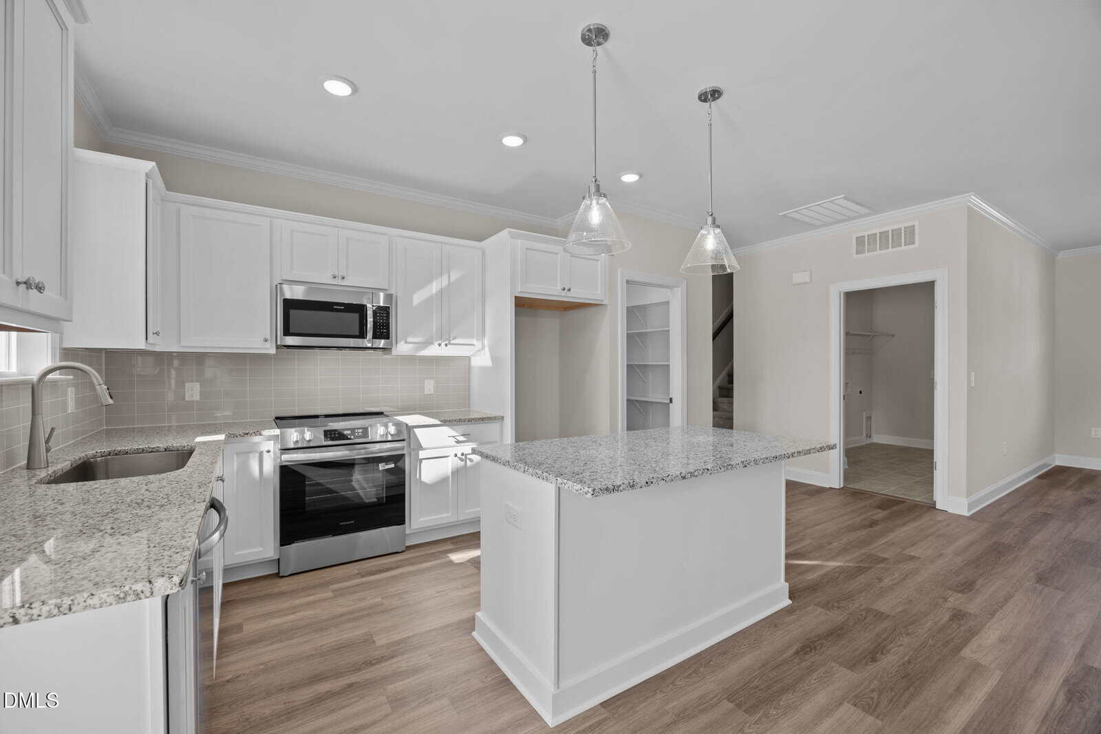Modern kitchen with white cabinets, granite countertops, stainless steel appliances, a center island with pendant lights, tile backsplash, and wood-style flooring. Open shelving and a pantry are visible in the background.